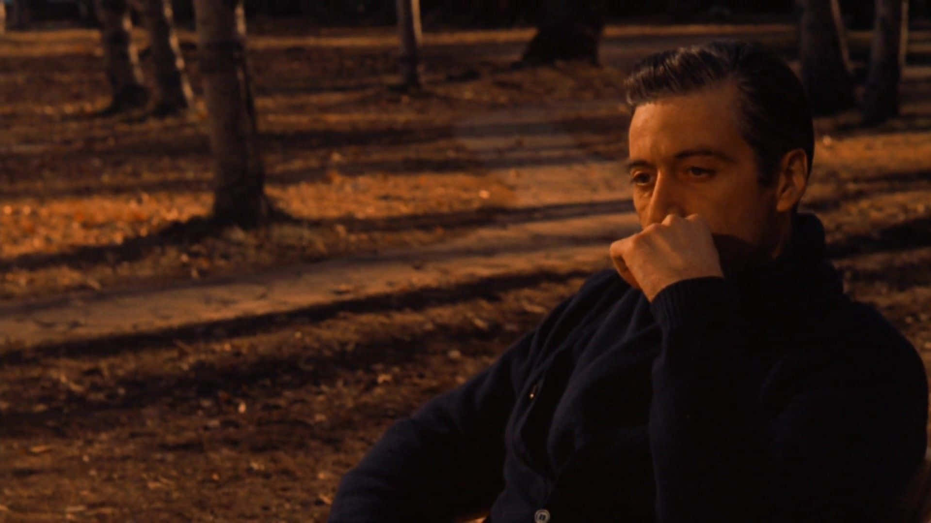 The Godfather 桌布 壁紙 — 一個穿著深色毛衣的男人在黃昏的公園裡沉思，手靠近嘴邊，沐浴在溫暖的金色光芒中。