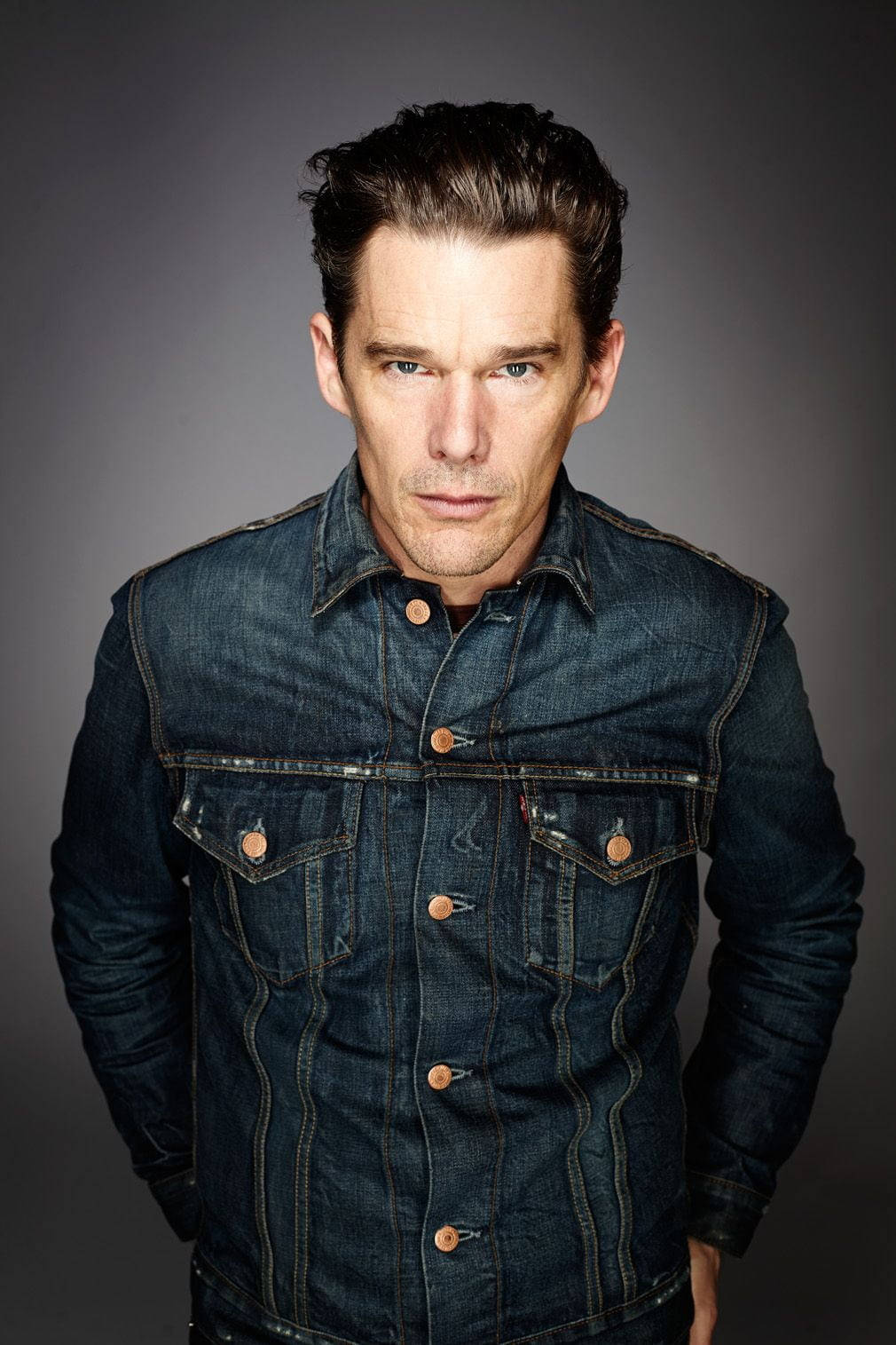 Celebrity 桌布 壁紙 — 一個穿著深色牛仔外套的男人，在柔和的灰色攝影棚背景前專注地凝視。
