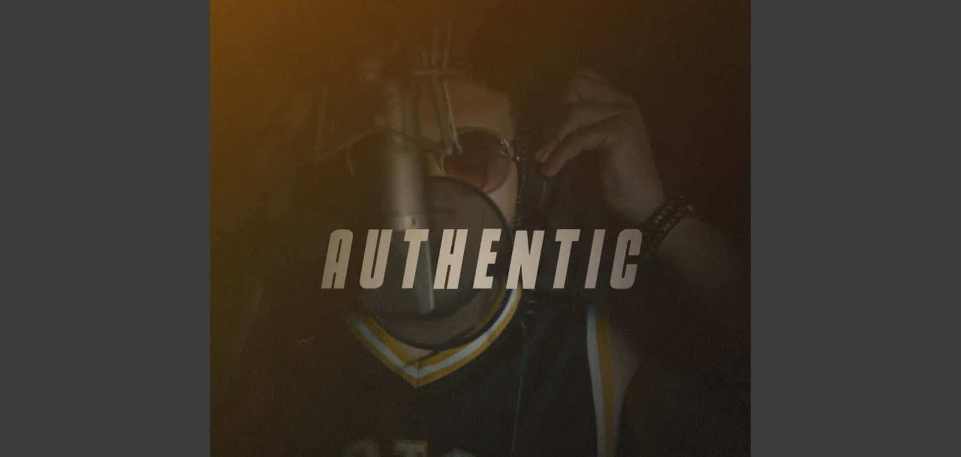 Authentic 桌布 壁紙 — 一個穿著深色球衣的人在溫暖金色燈光下調整太陽眼鏡，上面重疊了「真實」這個字。