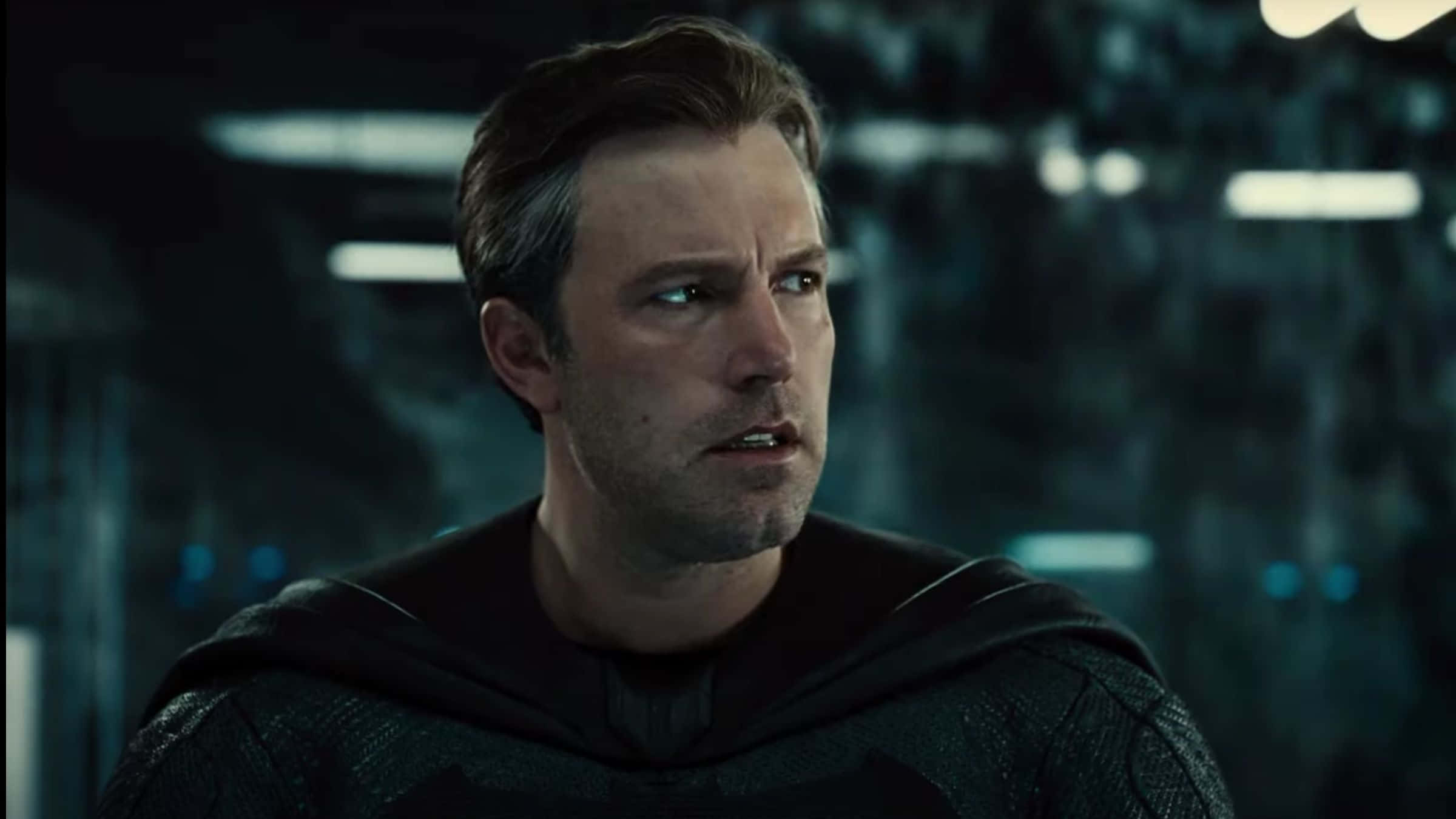 Ben Affleck 桌布 壁紙 — 一個穿著深色紋理斗篷的男人在昏暗的未來場景中，專注地向前凝視，周圍有發光的藍色燈光。