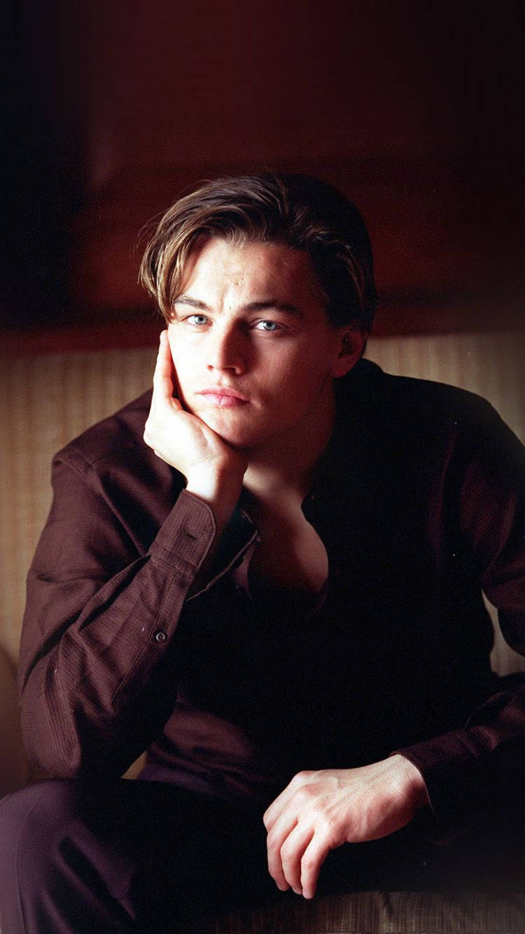 Dicaprio 桌布 壁紙 — 一個穿著深色襯衫的年輕男子，在暖色調模糊背景前，用手托著下巴，神情沉思。