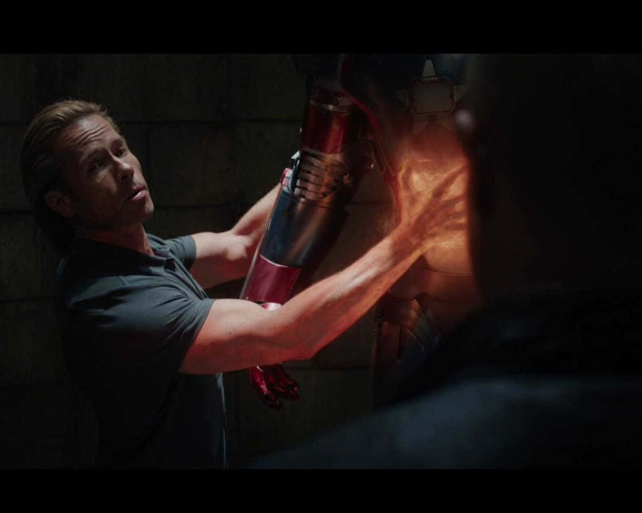 Iron Man Vs Killian 桌布 壁紙 — 一個穿著深色襯衫的男人在光線昏暗的石牆健身房裡，用一個發光的紅色沙袋進行激烈訓練。