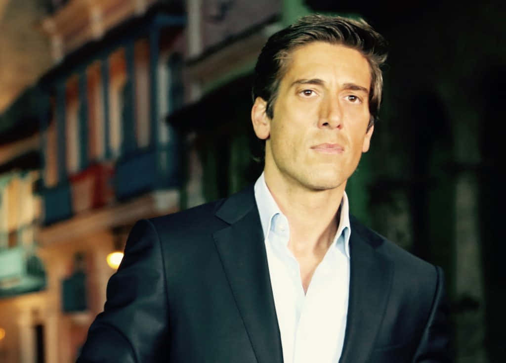 Handsome Man 桌布 壁紙 — 一個穿著深色西裝和淺色襯衫的男人，自信地站在柔和模糊的城市夜景背景前，背景有溫暖發光的燈光。