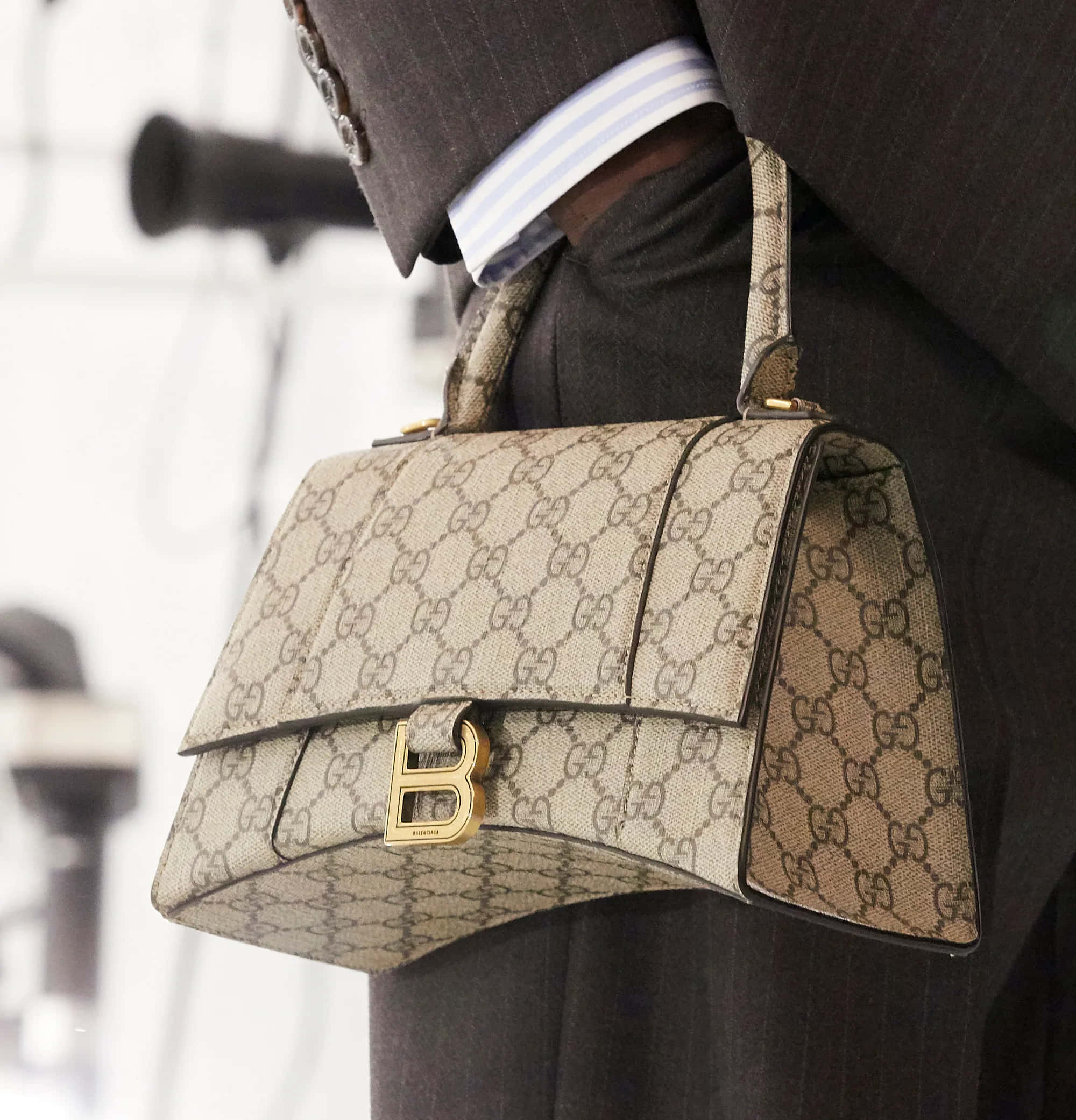 Gucci 桌布 壁紙 — 一個穿著深色西裝的人拿著一個米色Gucci手袋，帶有交錯的G圖案和金色五金件。