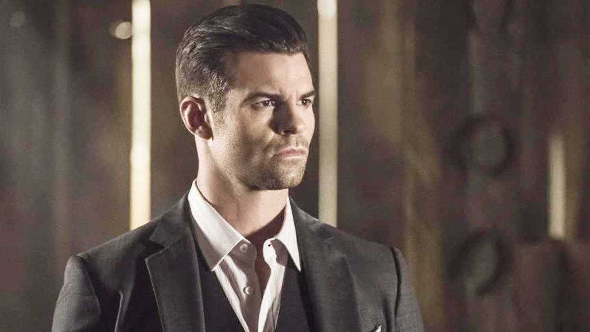 elijah mikaelson 桌布 壁紙 — 一個穿著深色西裝的男人站在一個光線昏暗的房間裡，身後有垂直的光條。