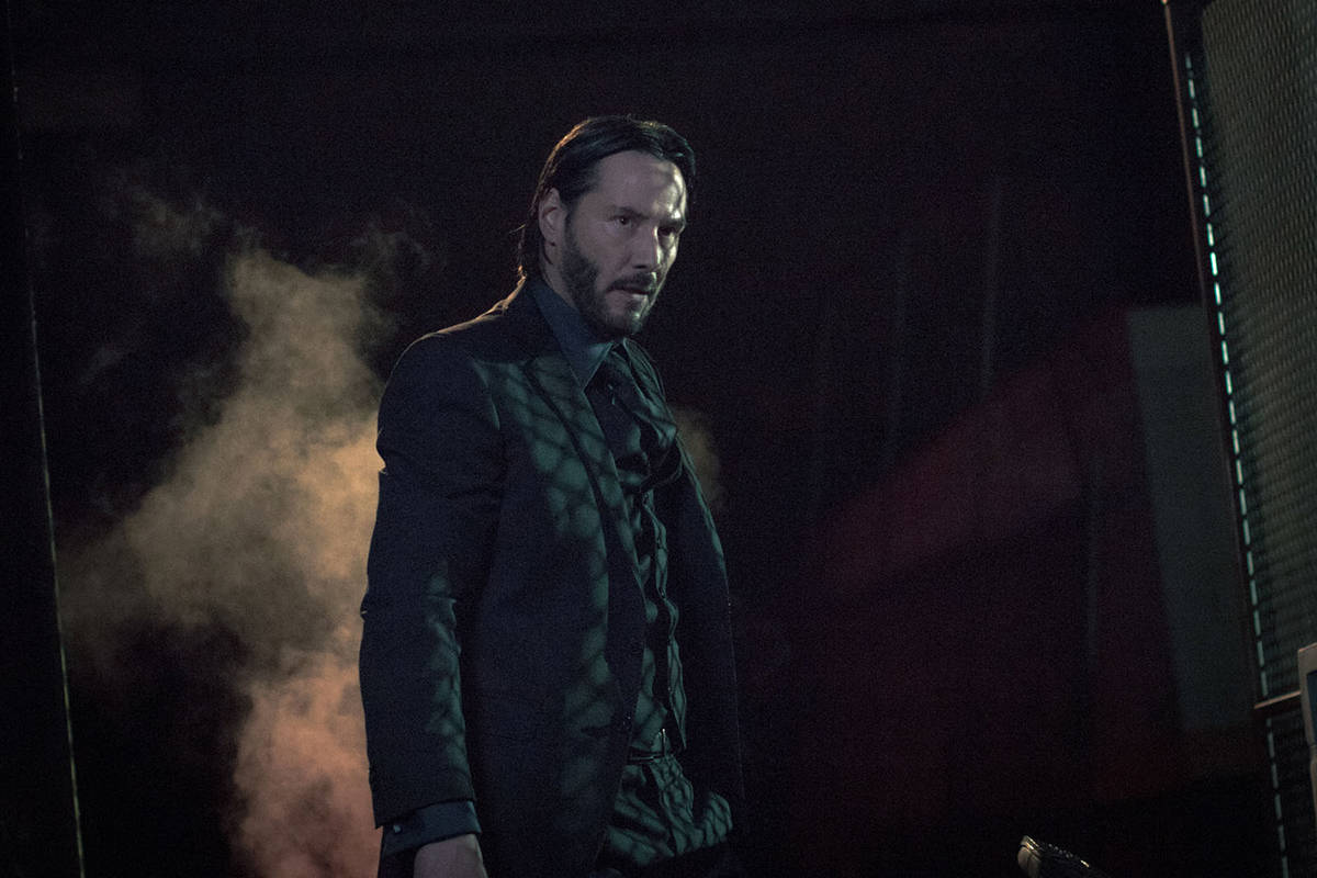 John Wick 桌布 壁紙 — 一個穿著深色西裝的男人站在煙霧瀰漫、燈光昏暗的房間裡，表情專注而強烈。