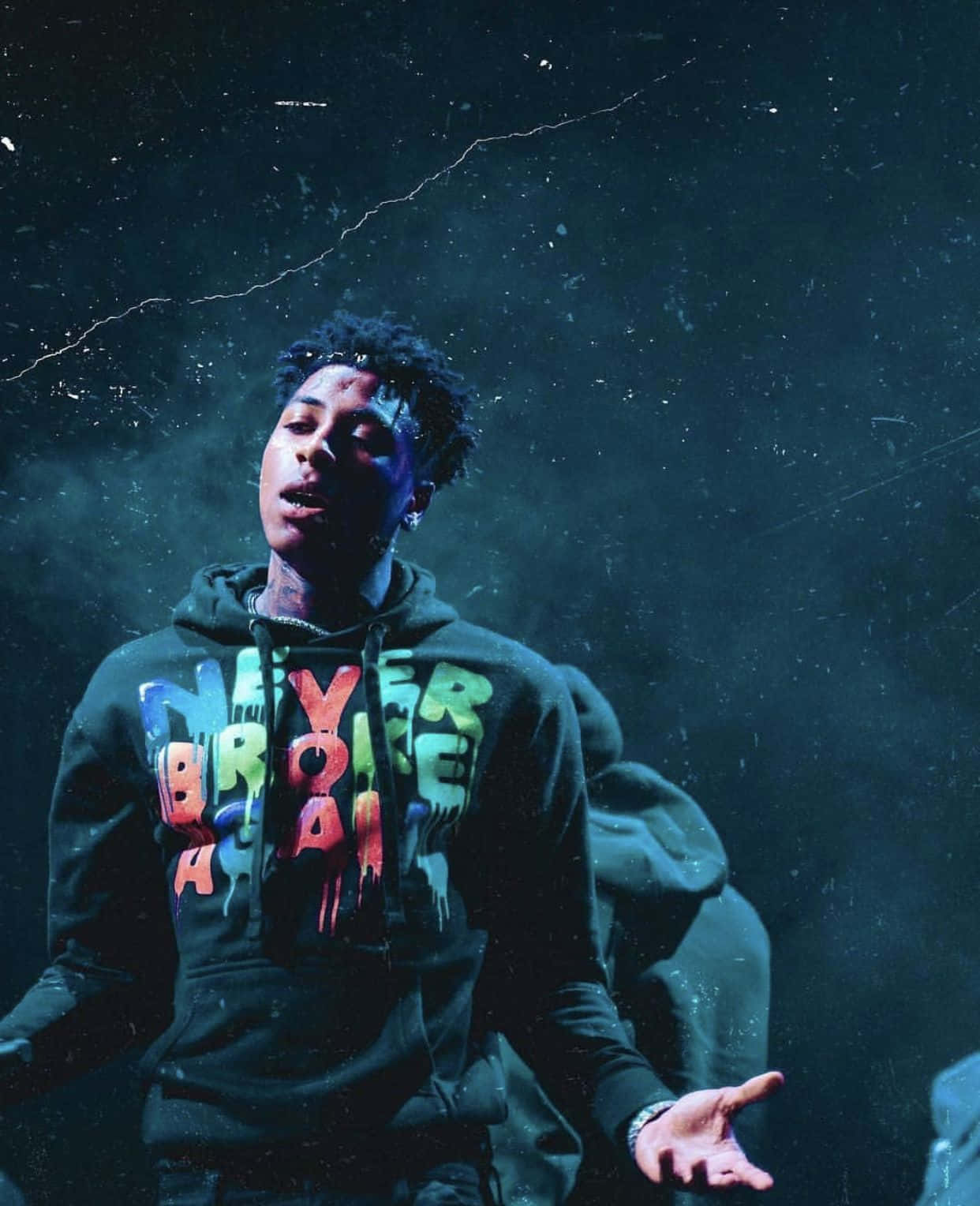 Youngboy 桌布 壁紙 — 一個穿著深色連帽衫、帶有彩色滴落文字的年輕男子，站在煙霧繚繞的藍色背景前，燈光效果戲劇化。