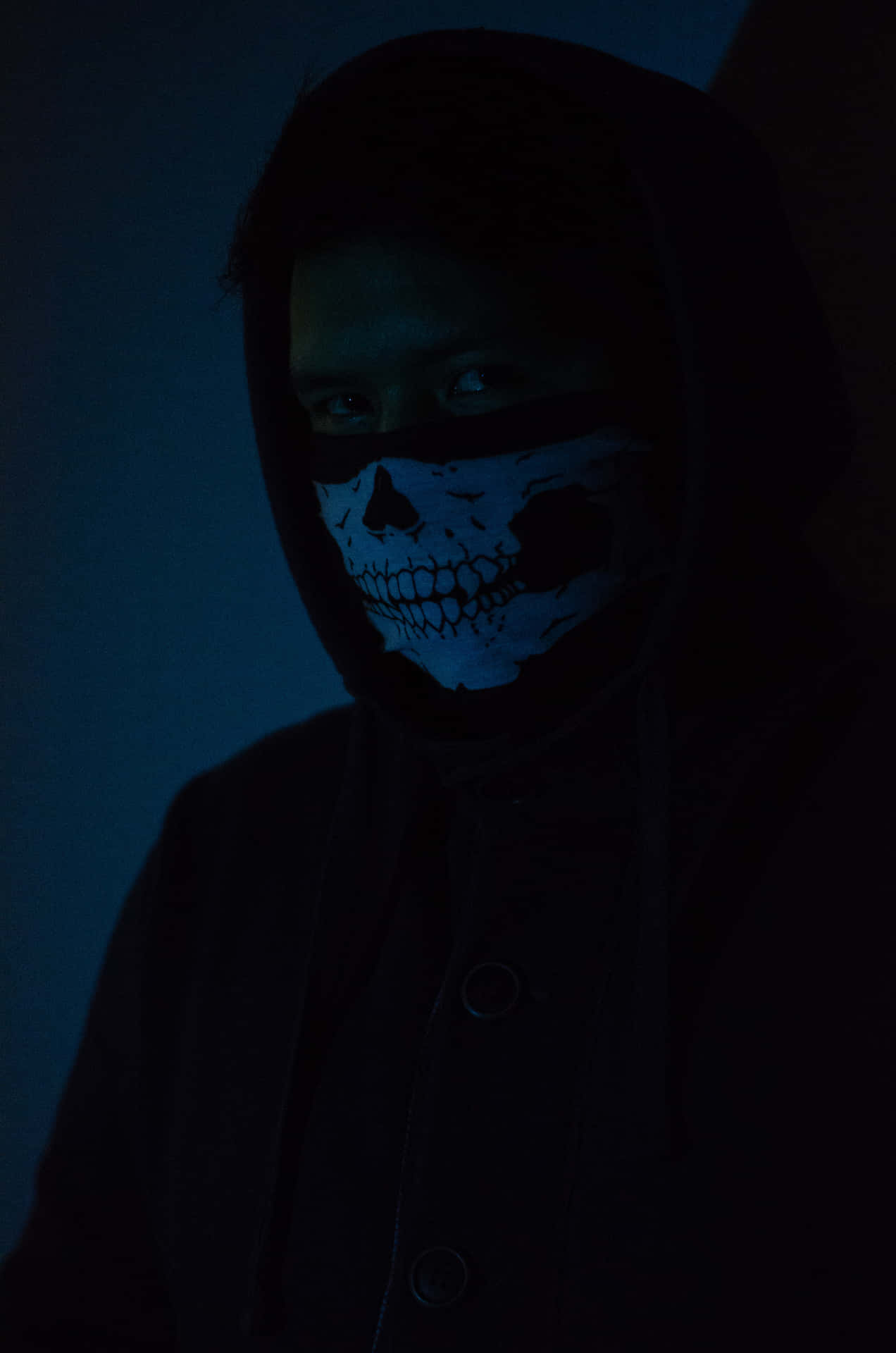 Man 桌布 壁紙 — 一個穿著深色連帽衫的人，在陰暗的房間裡，在詭異的藍光下戴著發光的骷髏面具。