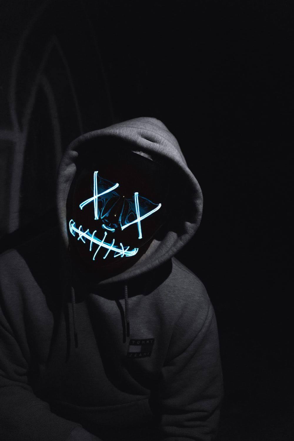 Mask 桌布 壁紙 — 一個穿著深色連帽衫的人，在黑色背景下戴著發光藍色LED面具，面具上有縫合的嘴巴和X形眼睛。