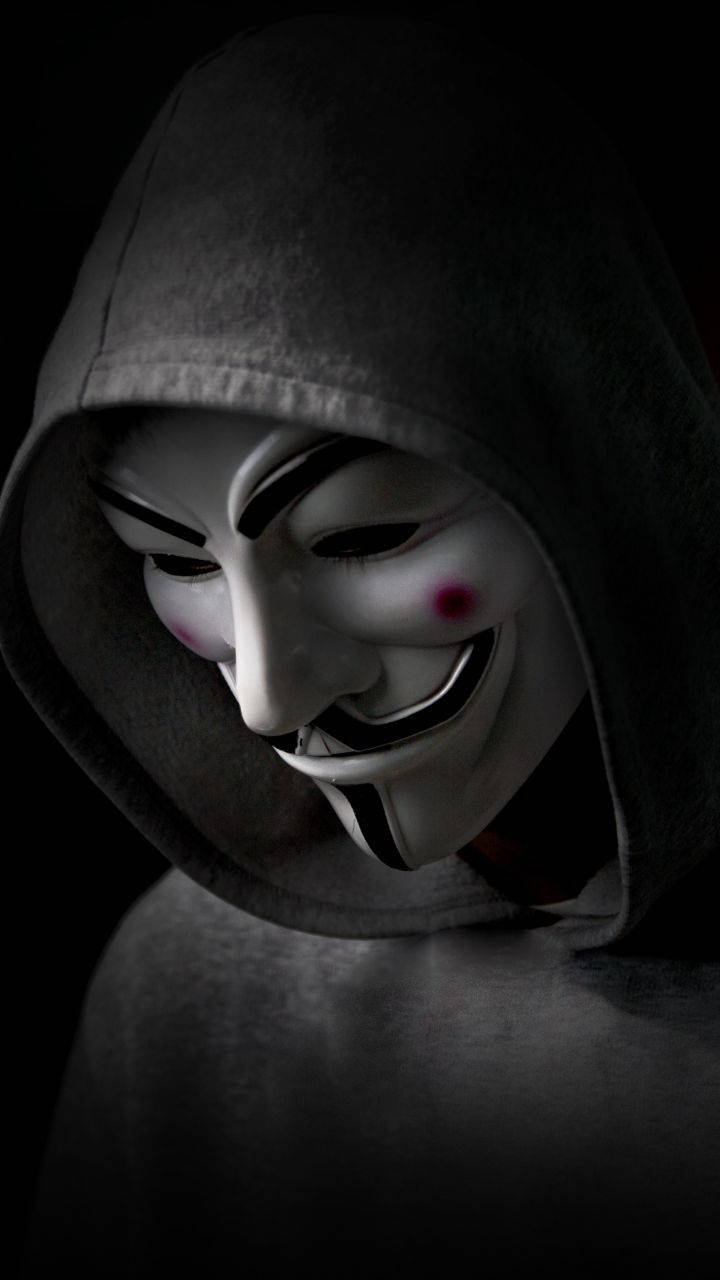 Mask 桌布 壁紙 — 一個穿著深色連帽衫的人，在黑色背景上戴著帶有紅色臉頰標記的白色蓋伊·福克斯面具。