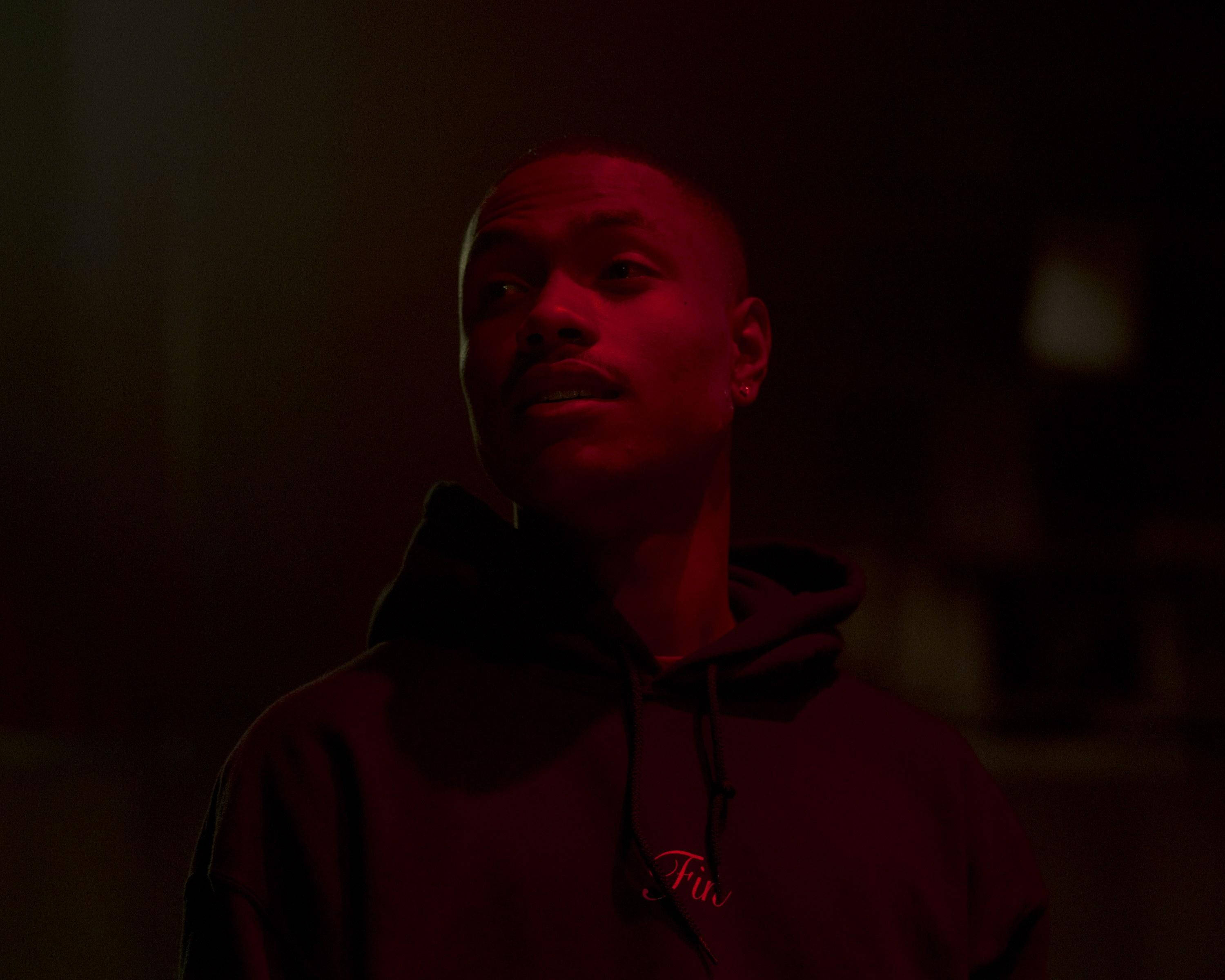 Steve Lacy 桌布 壁紙 — 一個穿著深色連帽衫的男人在陰暗的房間裡，在強烈的紅光下向上凝視。