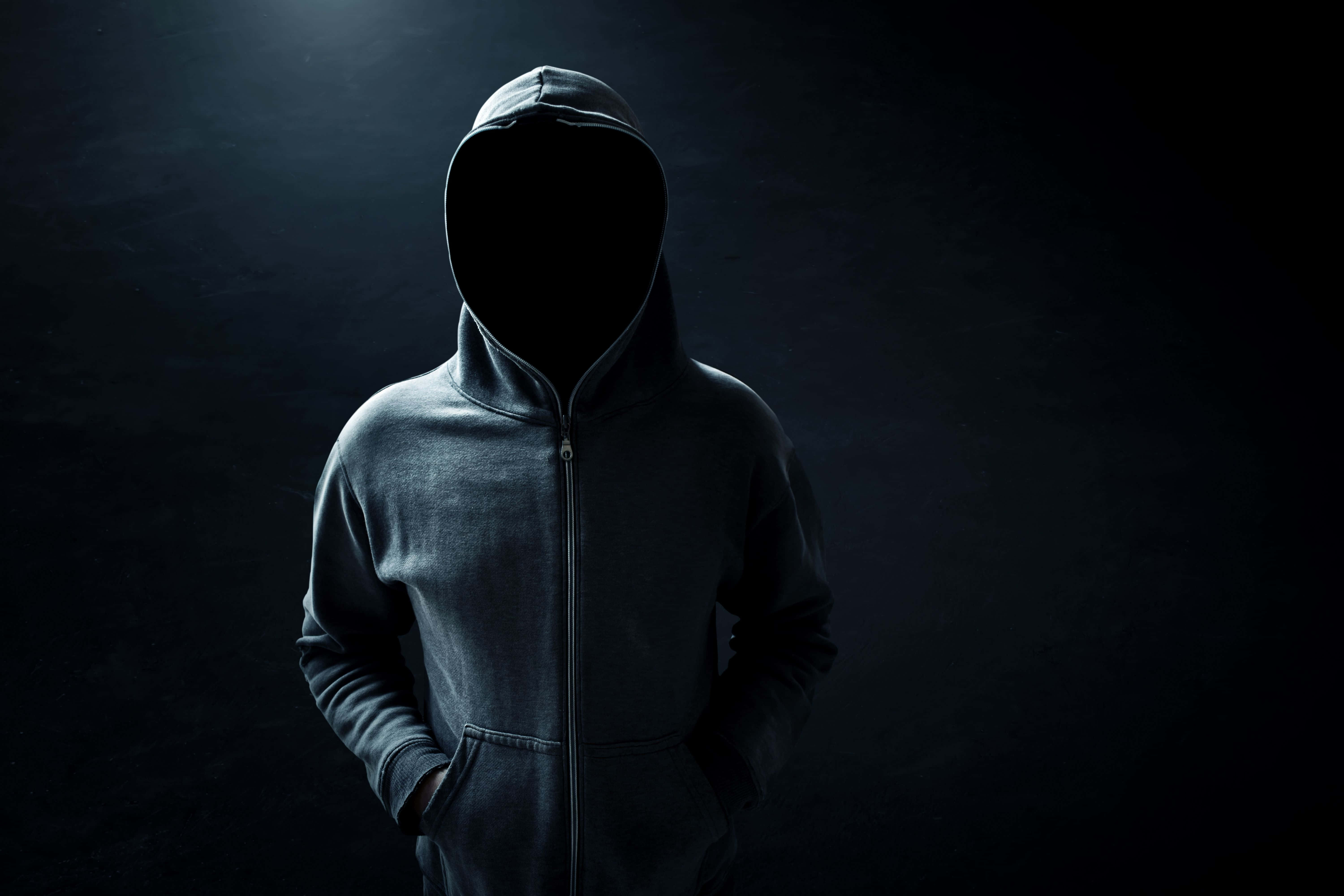 Hoodie 桌布 壁紙 — 一個穿著深色連帽衫的神秘身影站在昏暗的空間中，單一聚光燈突顯了衣物的質感和形態。
