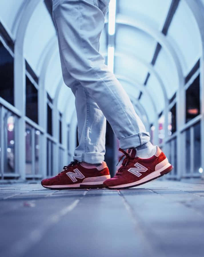 Red Shoes 桌布 壁紙 — 一個穿著淺色牛仔褲和紅色New Balance運動鞋的人，夜晚站在一個涼爽的藍色燈光拱形通道中。