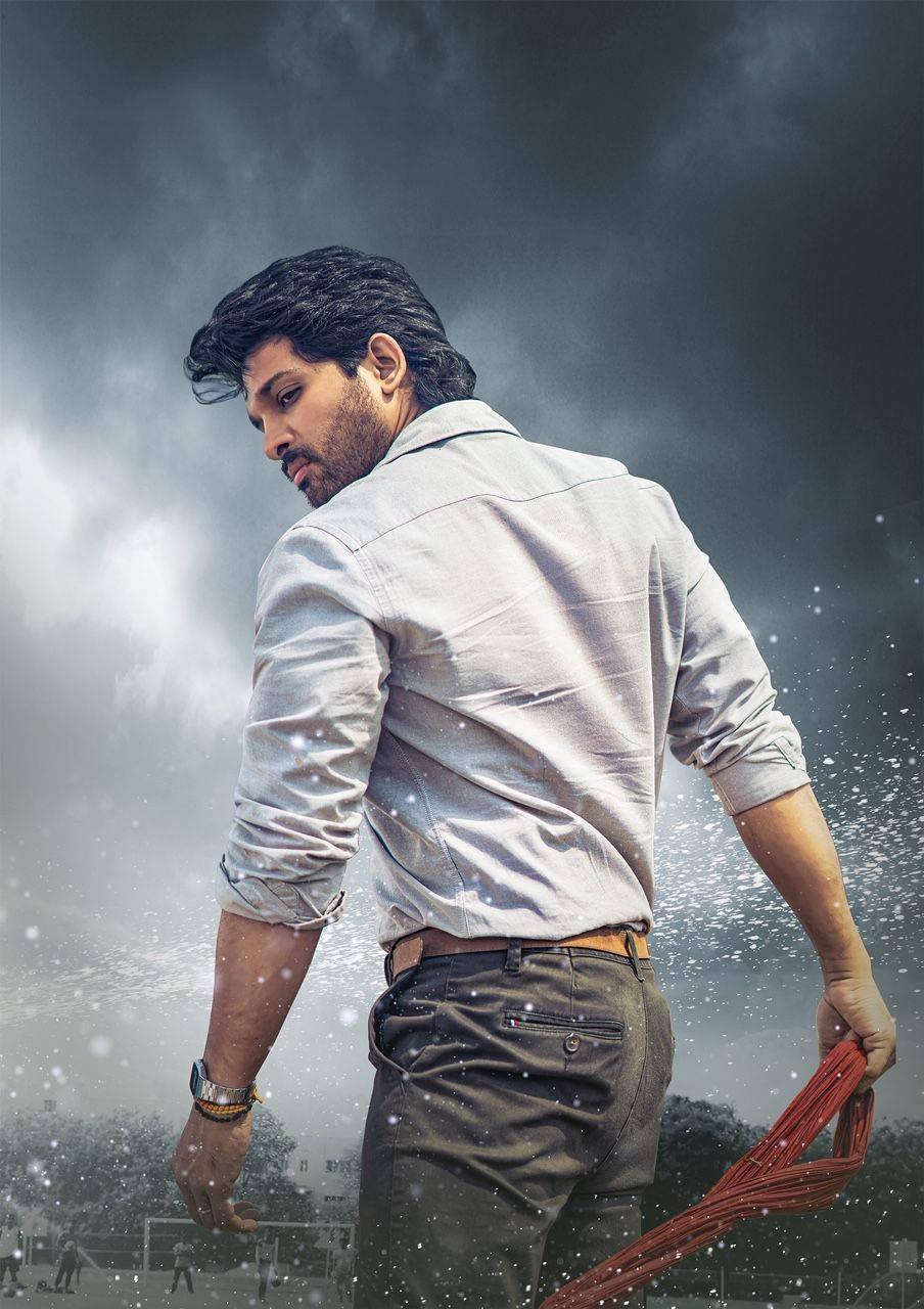 Allu Arjun 桌布 壁紙 — 一個穿著淺色襯衫的男人在暴風雨的天空下走開，手持一個紅色物體，雪花在他周圍飄落。