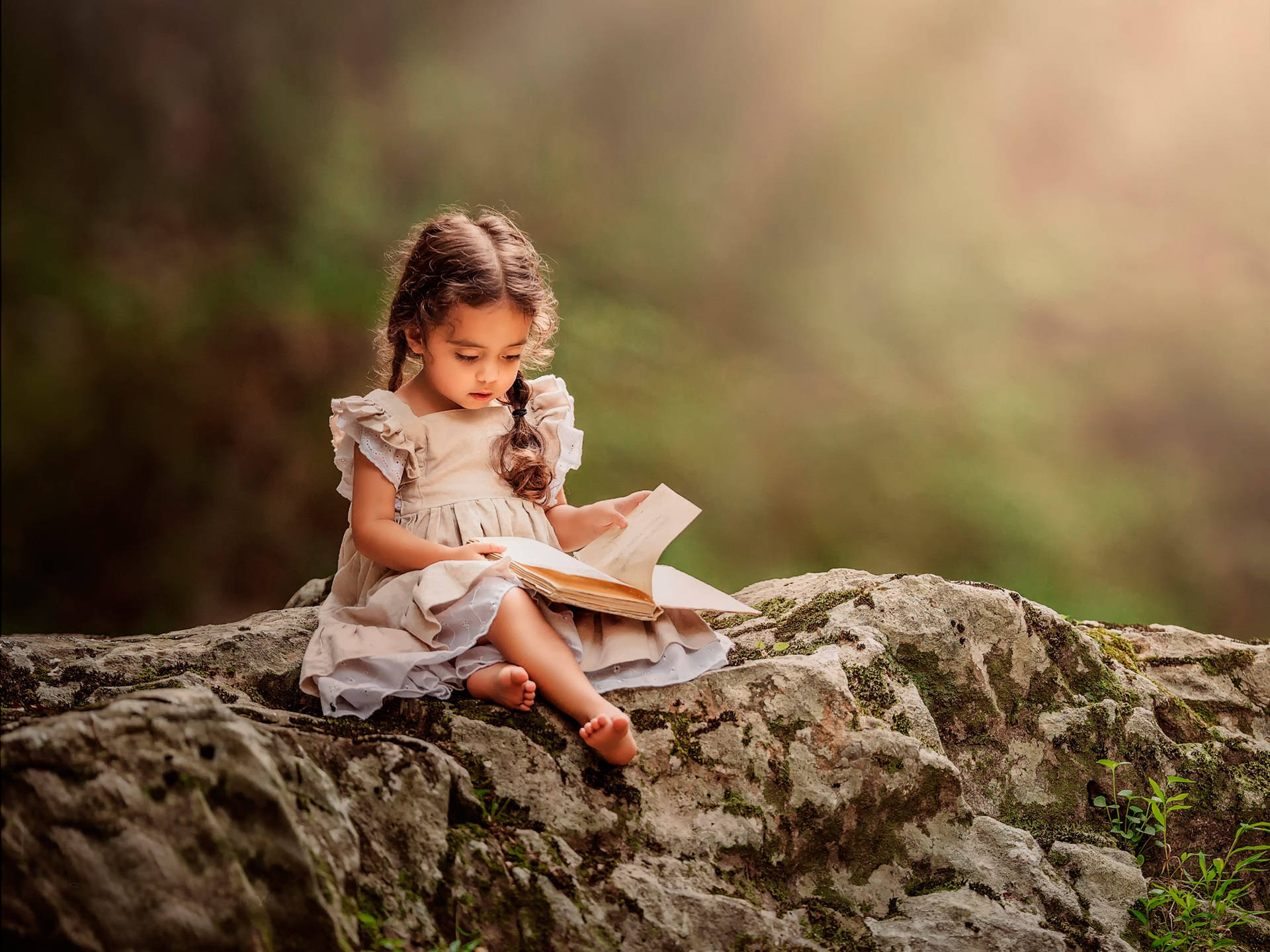 Reading 桌布 壁紙 — 一個穿著淺色連衣裙的小女孩赤腳坐在長滿苔蘚的石頭上讀書，金色的陽光透過她身後模糊的森林照射進來。