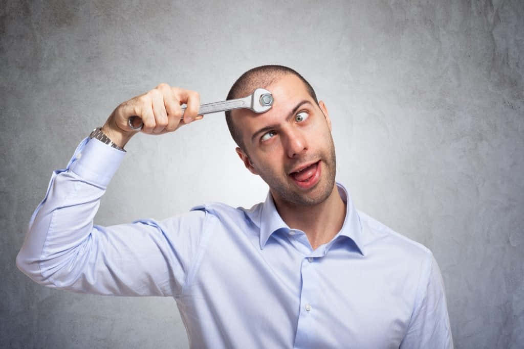 dumb 桌布 壁紙 — 一個穿著淺藍色襯衫的男人，在灰色牆前面，用一個震驚的表情將扳手拿在頭上。