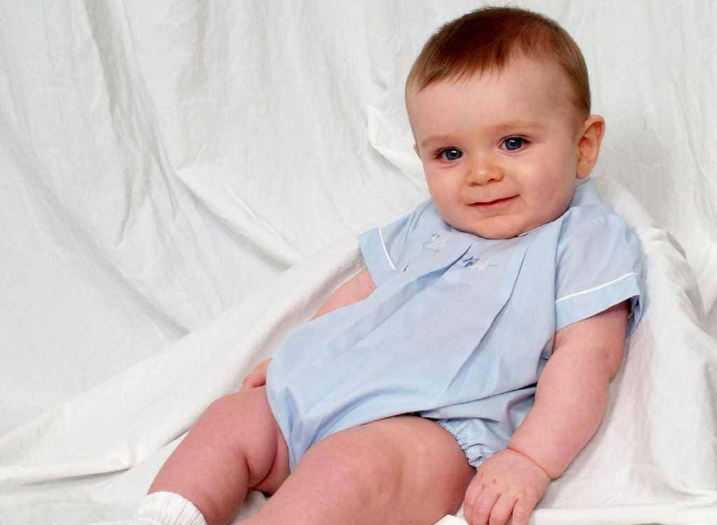 cute baby 桌布 壁紙 — 一個穿著淺藍色連身衣的胖嘟嘟嬰兒，坐在白色垂簾布料背景上，甜美地微笑。