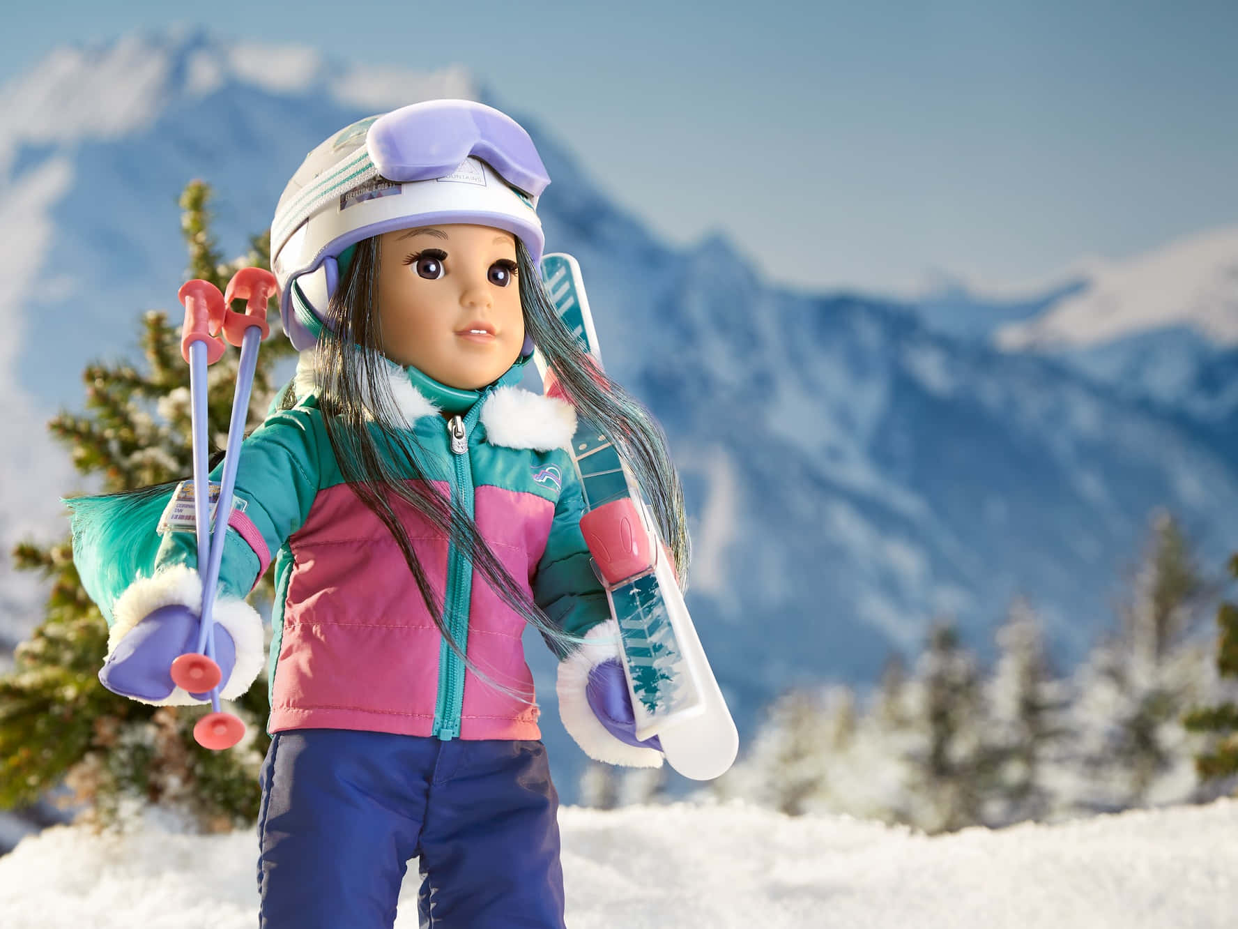 american girl 桌布 壁紙 — 一個穿著滑雪裝備的洋娃娃站在雪地上，手持滑雪板和滑雪杖，背景是白雪覆蓋的山脈和常青樹。