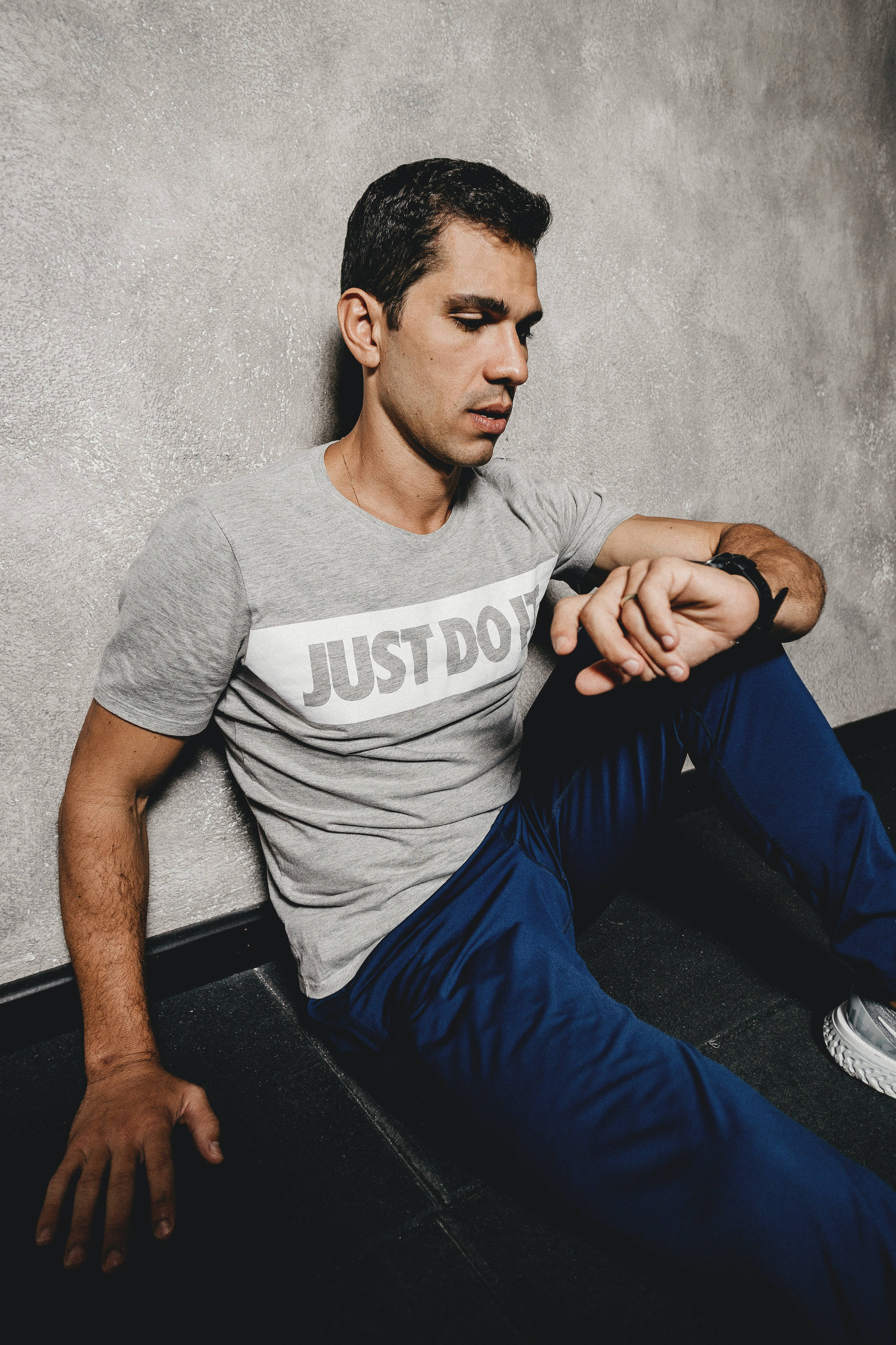 Mens Fashion 桌布 壁紙 — 一個穿著灰色「JUST DO IT」T恤的男人，帶著專注的強度靠著紋理牆壁坐著。