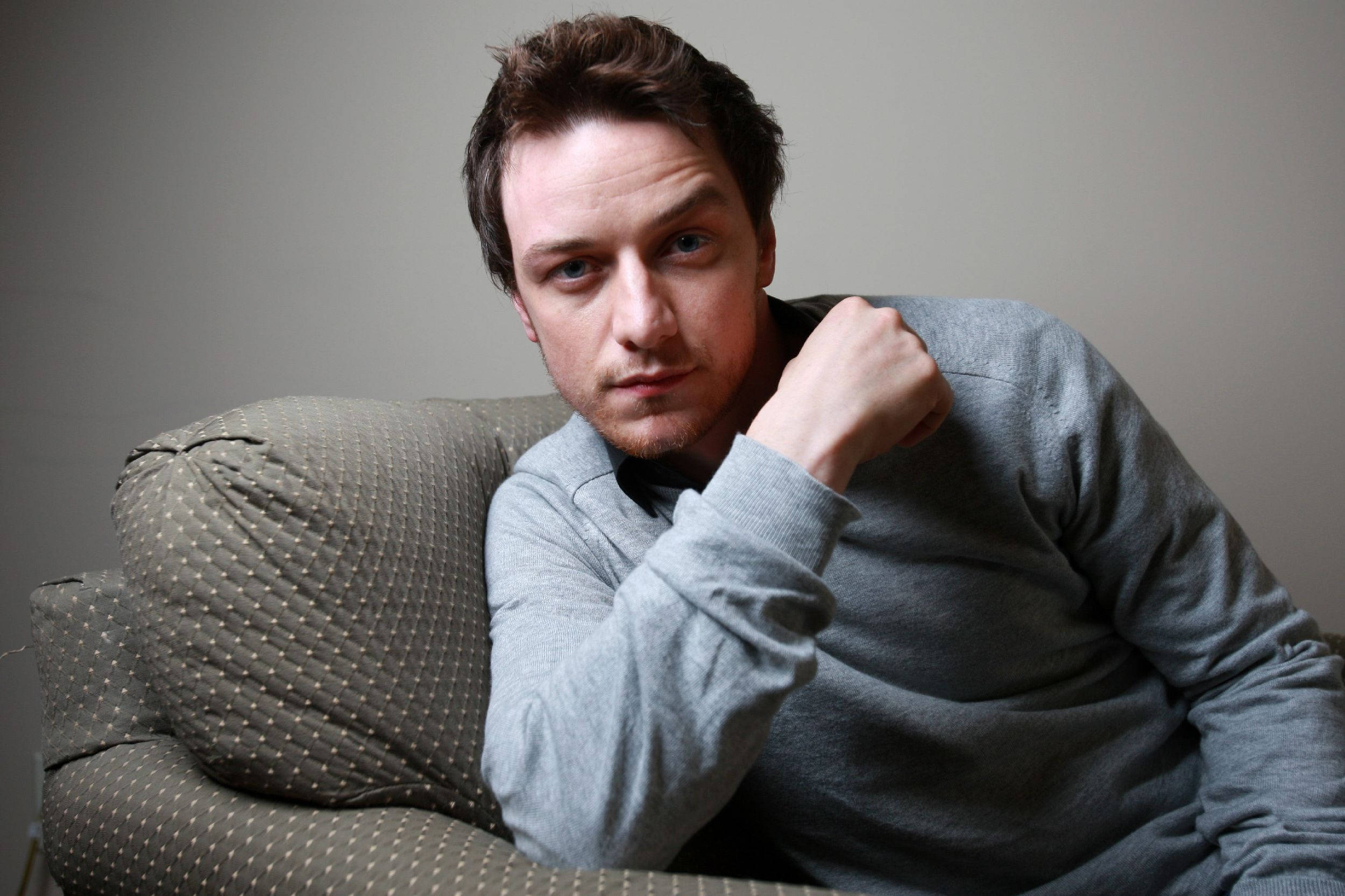 Celebrity 桌布 壁紙 — 一個穿著灰色毛衣的男人靠在一張有圖案的沙發上，對著一面素牆沉思。
