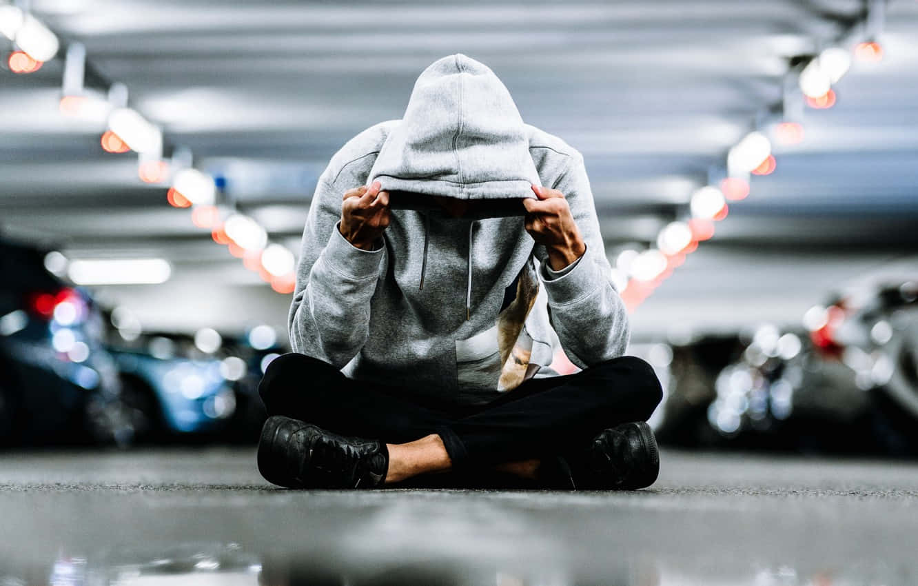 Men 桌布 壁紙 — 一個穿著灰色連帽衫的人盤腿坐在停車場地板上，雙手抱頭。