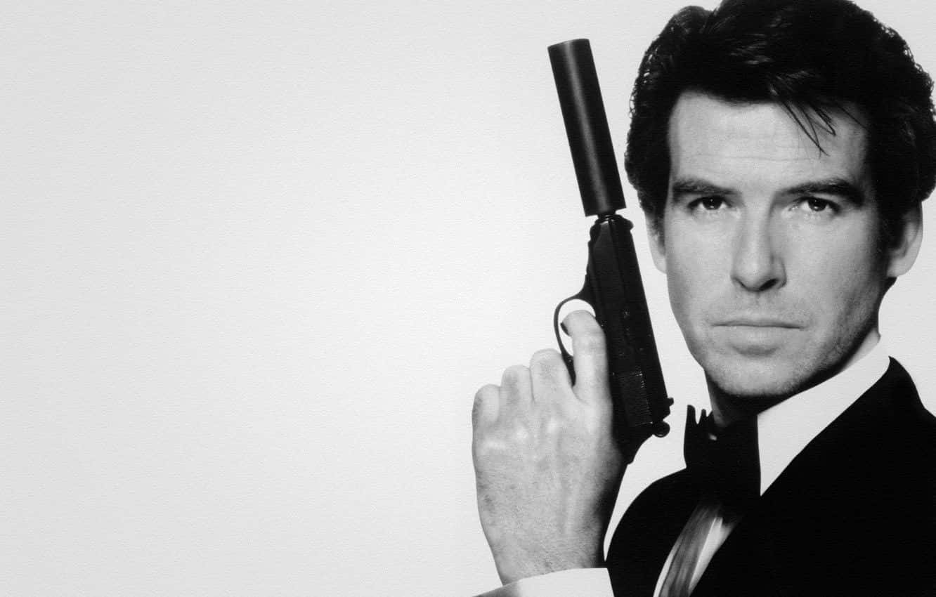 pierce brosnan 桌布 壁紙 — 一個穿著燕尾服的男人，手持消音手槍，神情嚴肅，背景簡潔的黑白肖像。