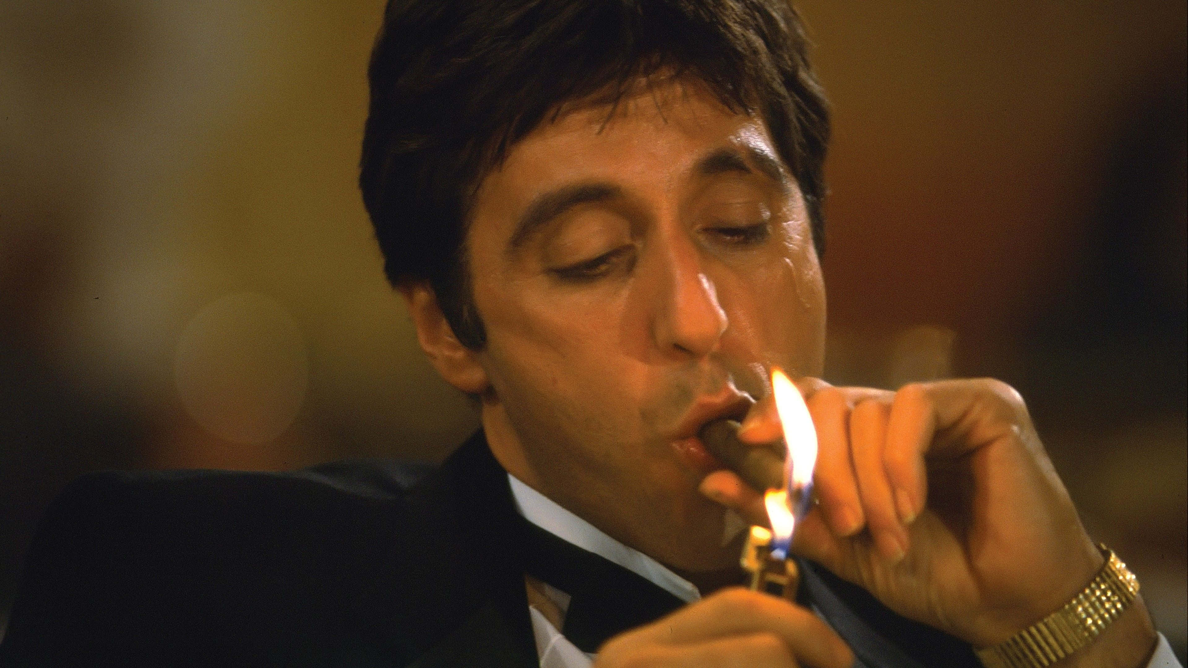 Scarface Desktop 桌布 壁紙 — 一個穿著燕尾服的男人在昏暗的房間裡用閃爍的打火機點燃雪茄。