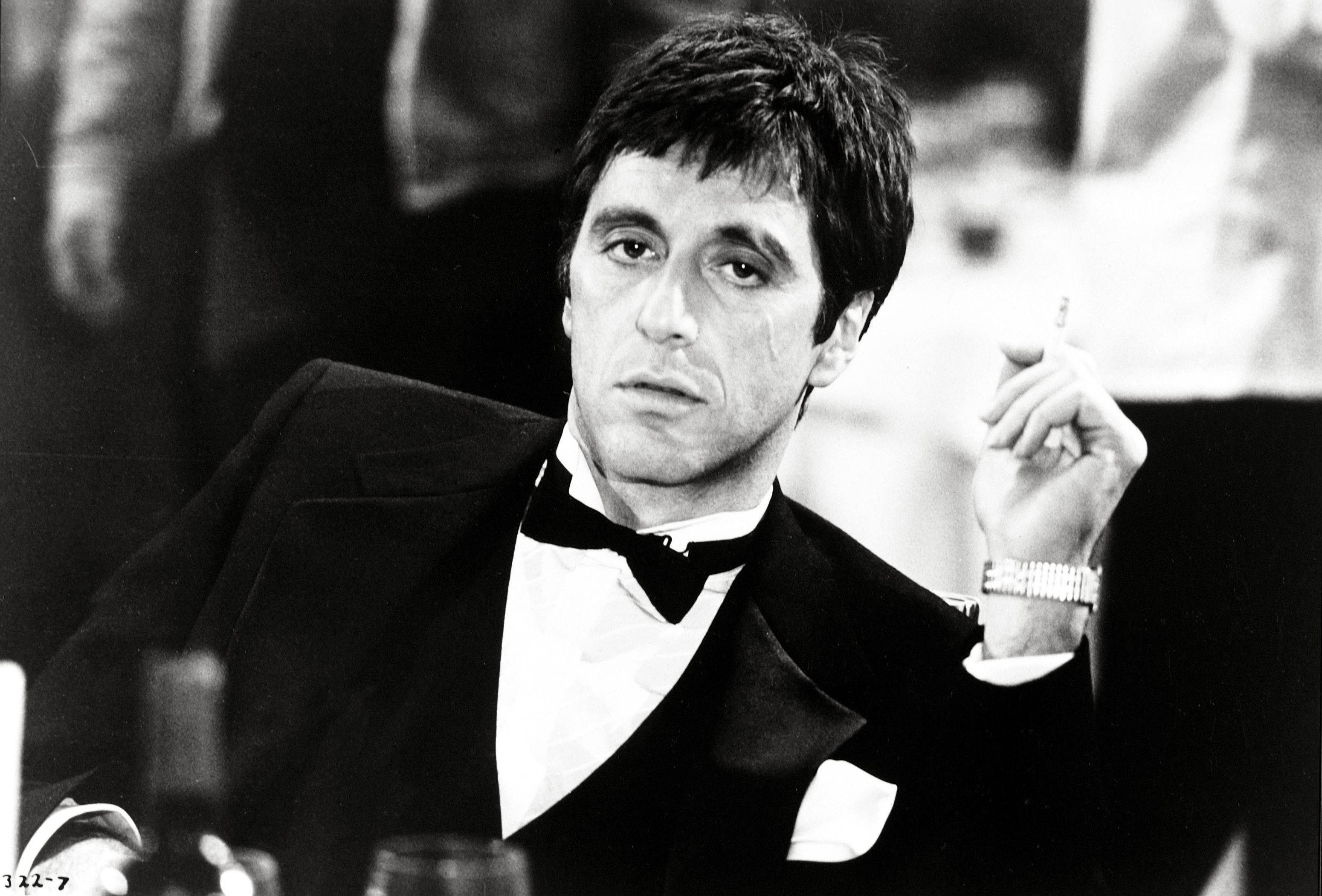 Al Pacino 桌布 壁紙 — 一個穿著燕尾服的男人在昏暗的房間裡拿著一支煙，表情嚴肅。
