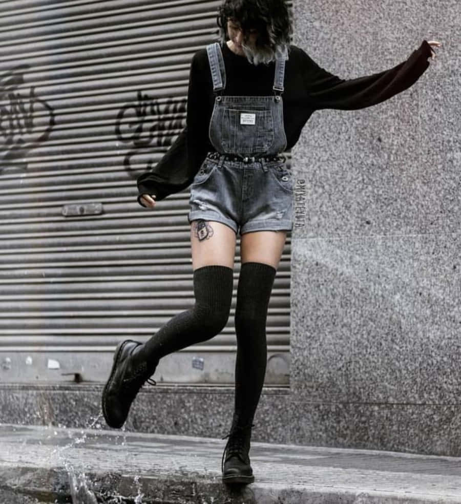 桌布 壁紙 — 一個穿著牛仔吊帶褲和黑色靴子的人，在濕漉漉的人行道上空跳躍，旁邊是佈滿塗鴉的金屬捲簾。