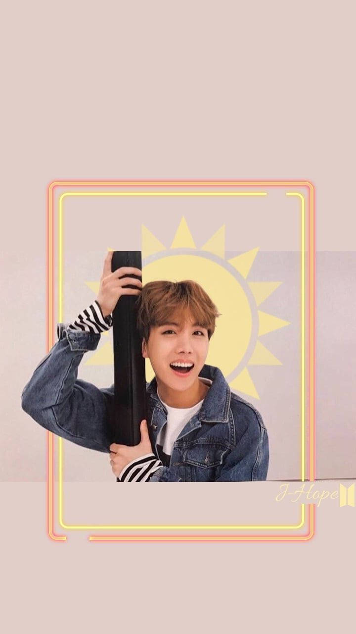 j-hope 桌布 壁紙 — 一個穿著牛仔外套的開朗年輕男子，在風格化的黃色太陽背景下，手持黑色桿子，露出燦爛的笑容。