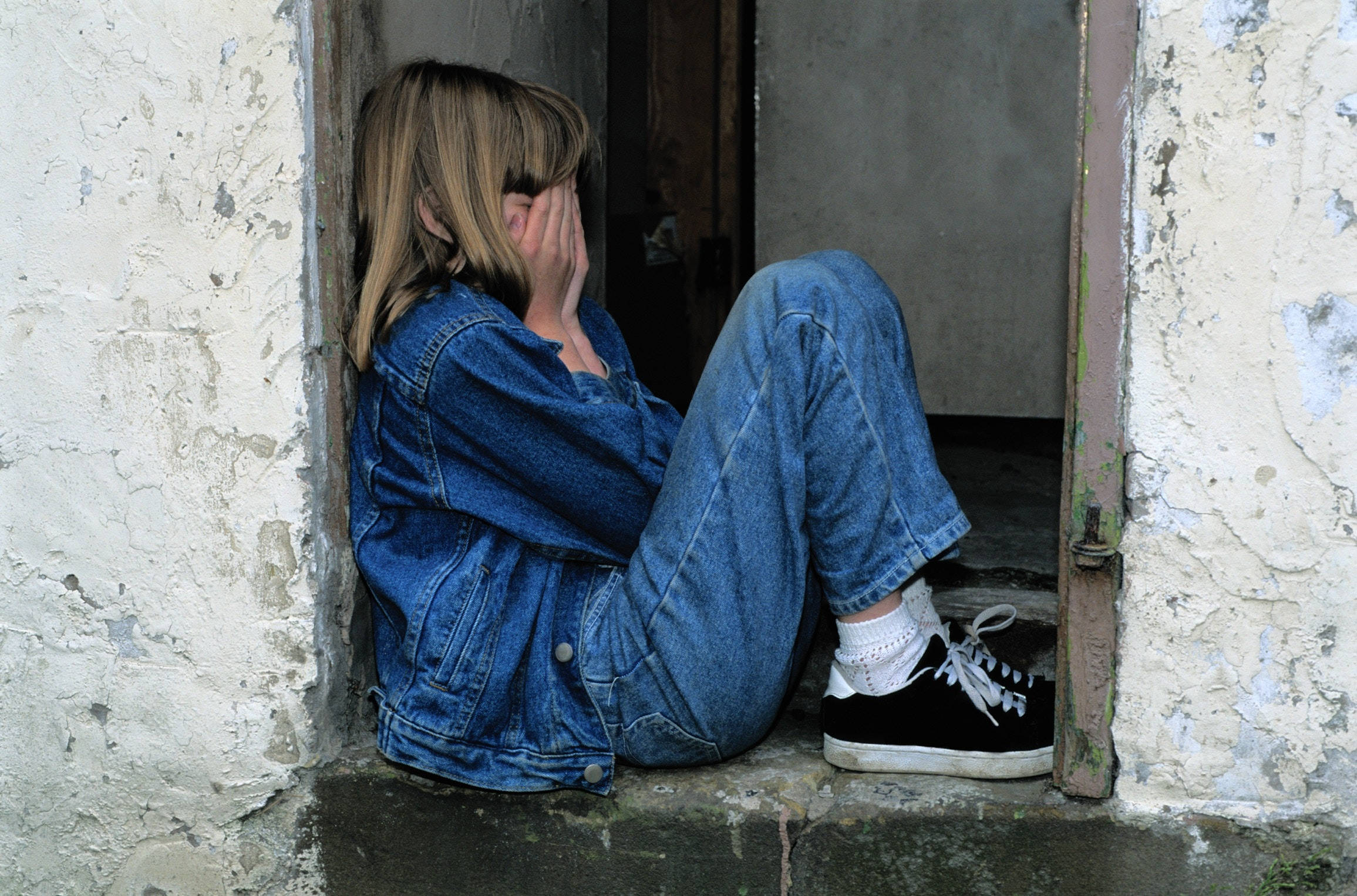 Depressed 桌布 壁紙 — 一個穿著牛仔布的女孩彎腰坐在門口，雙手掩面靠著風化的牆壁。