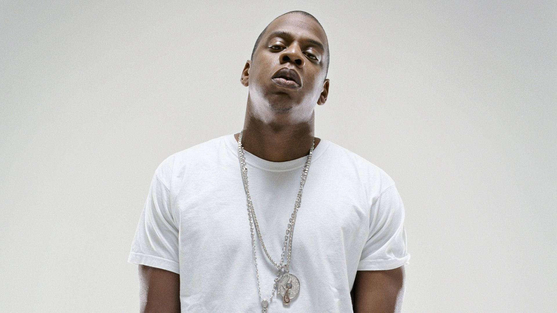 Jay-z 桌布 壁紙 — 一個穿著白色T恤和銀色鏈條的男人在純灰色背景上向上凝視。