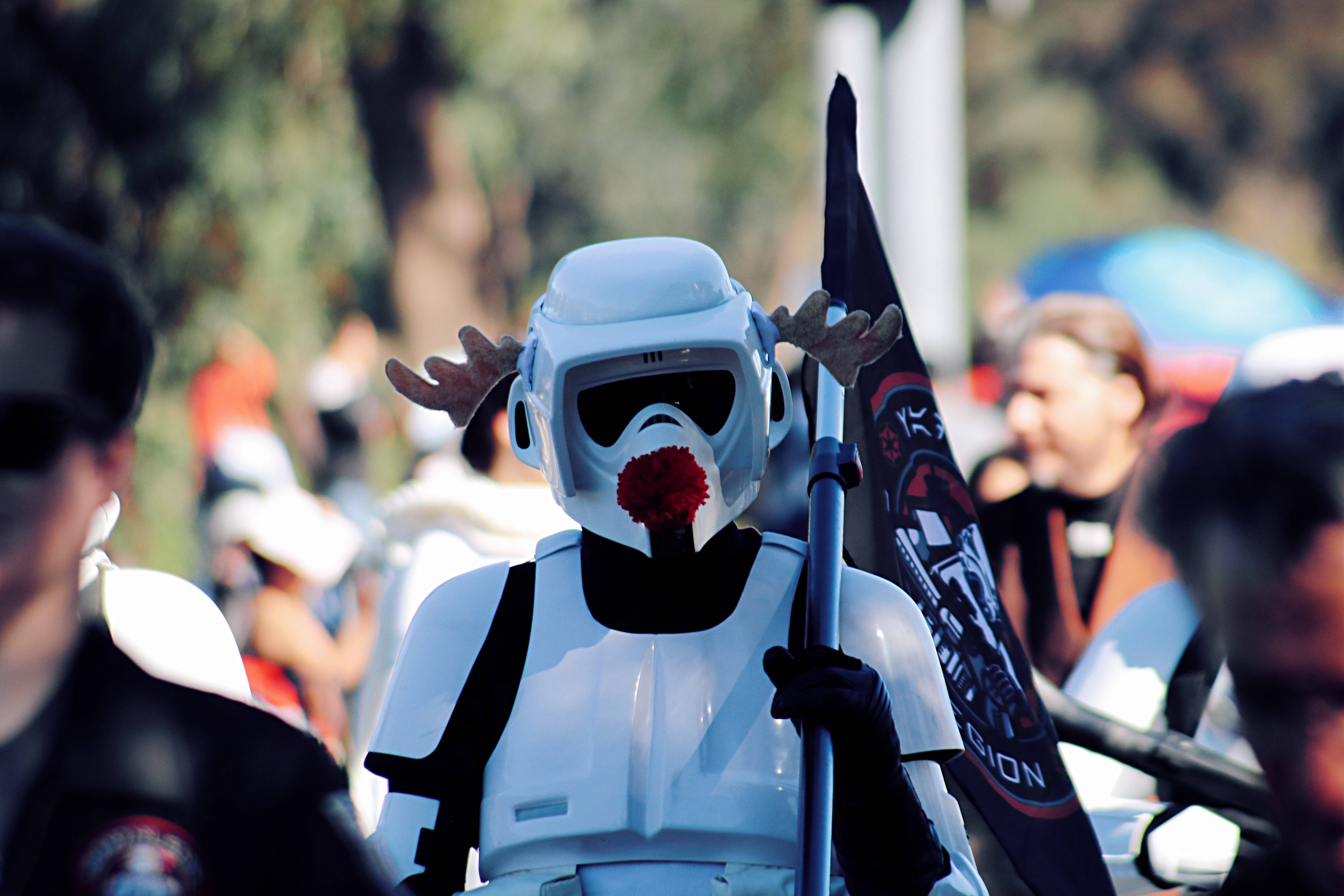 Star Wars Red 桌布 壁紙 — 一個穿著白色暴風兵服裝、頭上有鹿角、鼻子紅紅的人，在戶外聚會中手持旗幟站立。