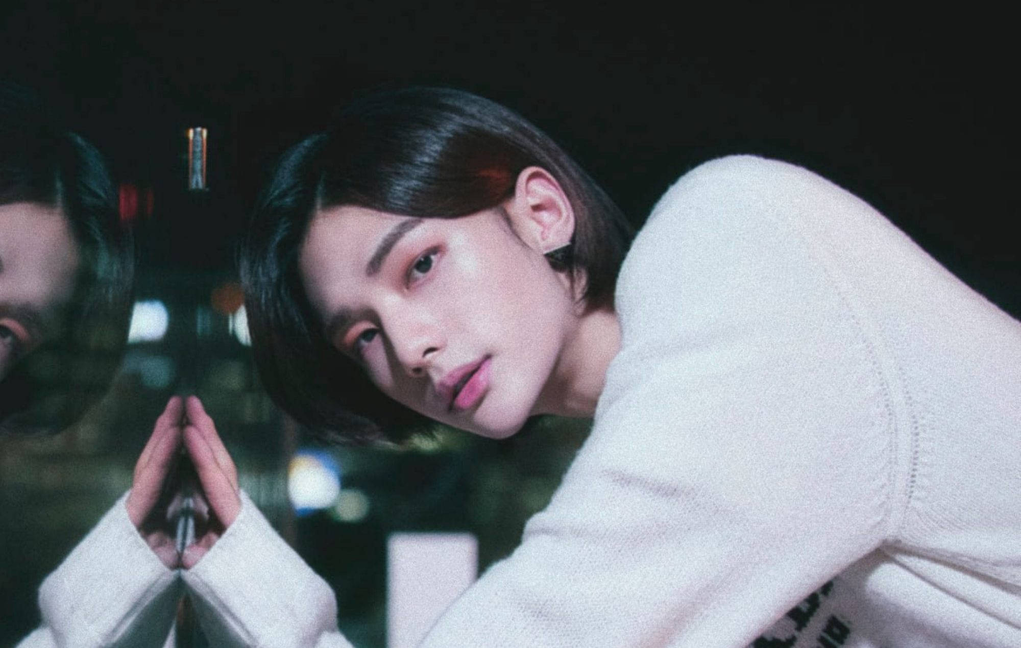 Stray Kids 桌布 壁紙 — 一個穿著白色毛衣的年輕人，在夜晚雙手合十，身體前傾，面向反光表面。