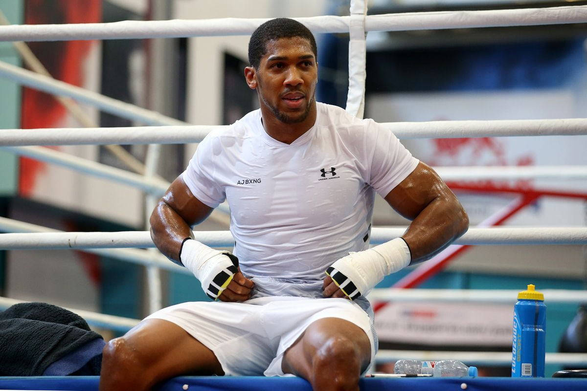 Anthony Joshua 桌布 壁紙 — 一個穿著白色裝備、汗流浹背的拳擊手坐在拳擊台的地板上，在訓練中看起來很專注。