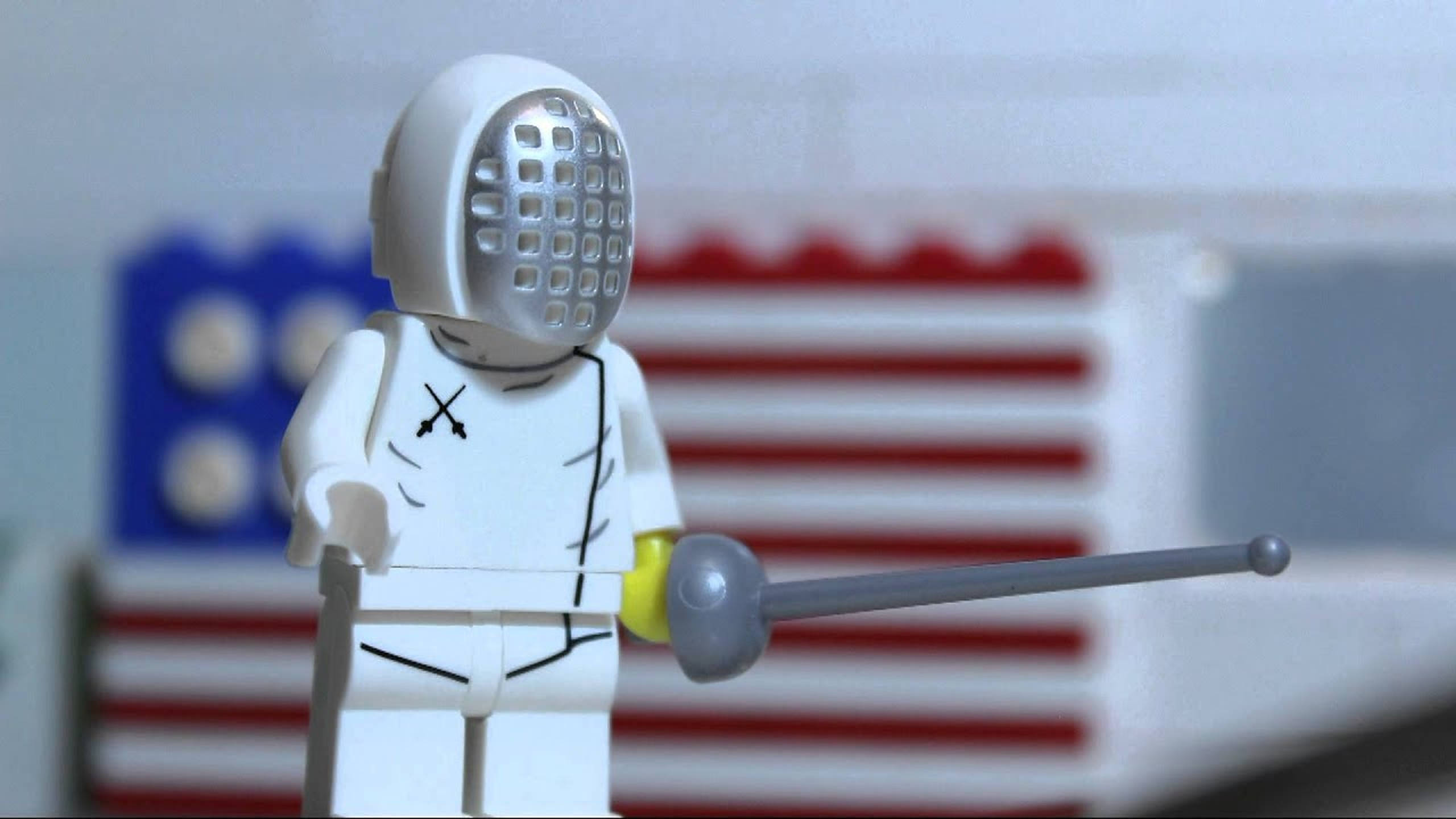 Fencing 桌布 壁紙 — 一個穿著白色裝備的LEGO擊劍人偶，手持花劍，背景是模糊的美國國旗。