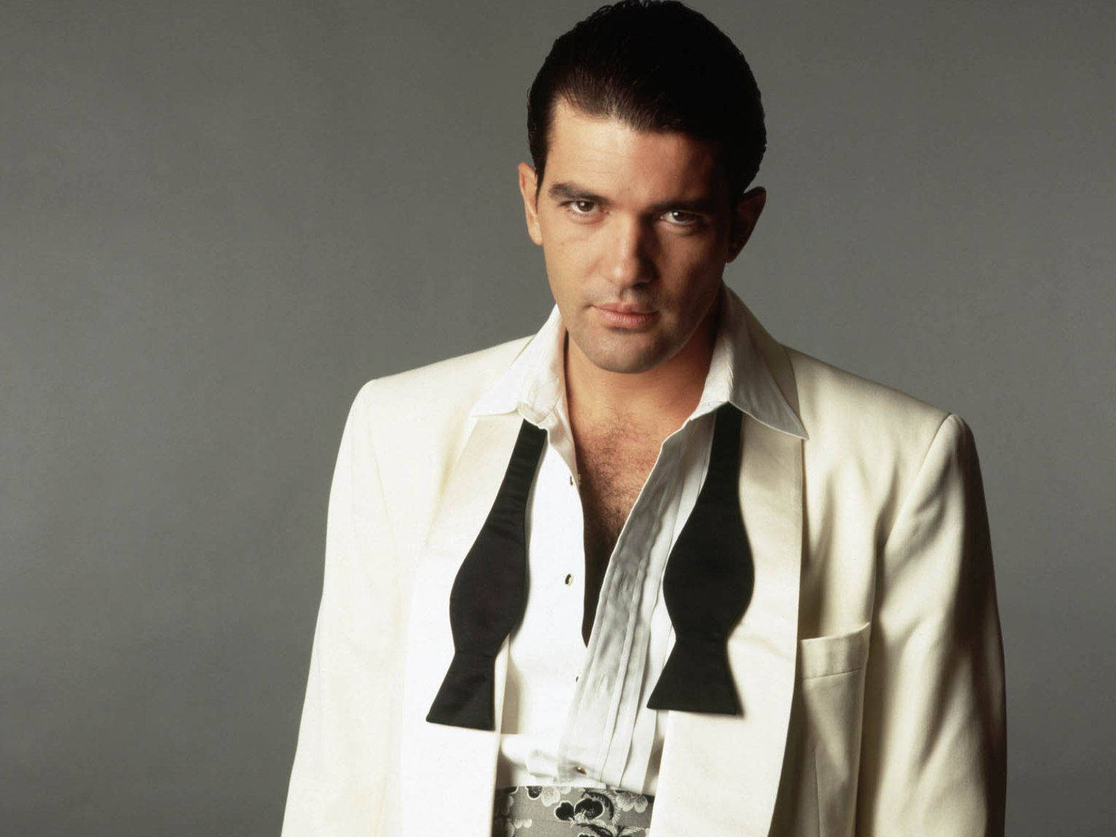 antonio banderas 桌布 壁紙 — 一個穿著白色西裝、黑色翻領的男人，在純灰色背景下凝視著。