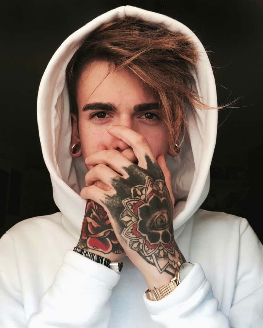 Tattoo Boy 桌布 壁紙 — 一個穿著白色連帽衫的年輕男子用刺青的手遮住嘴巴，眼睛在黑暗背景下顯得銳利。