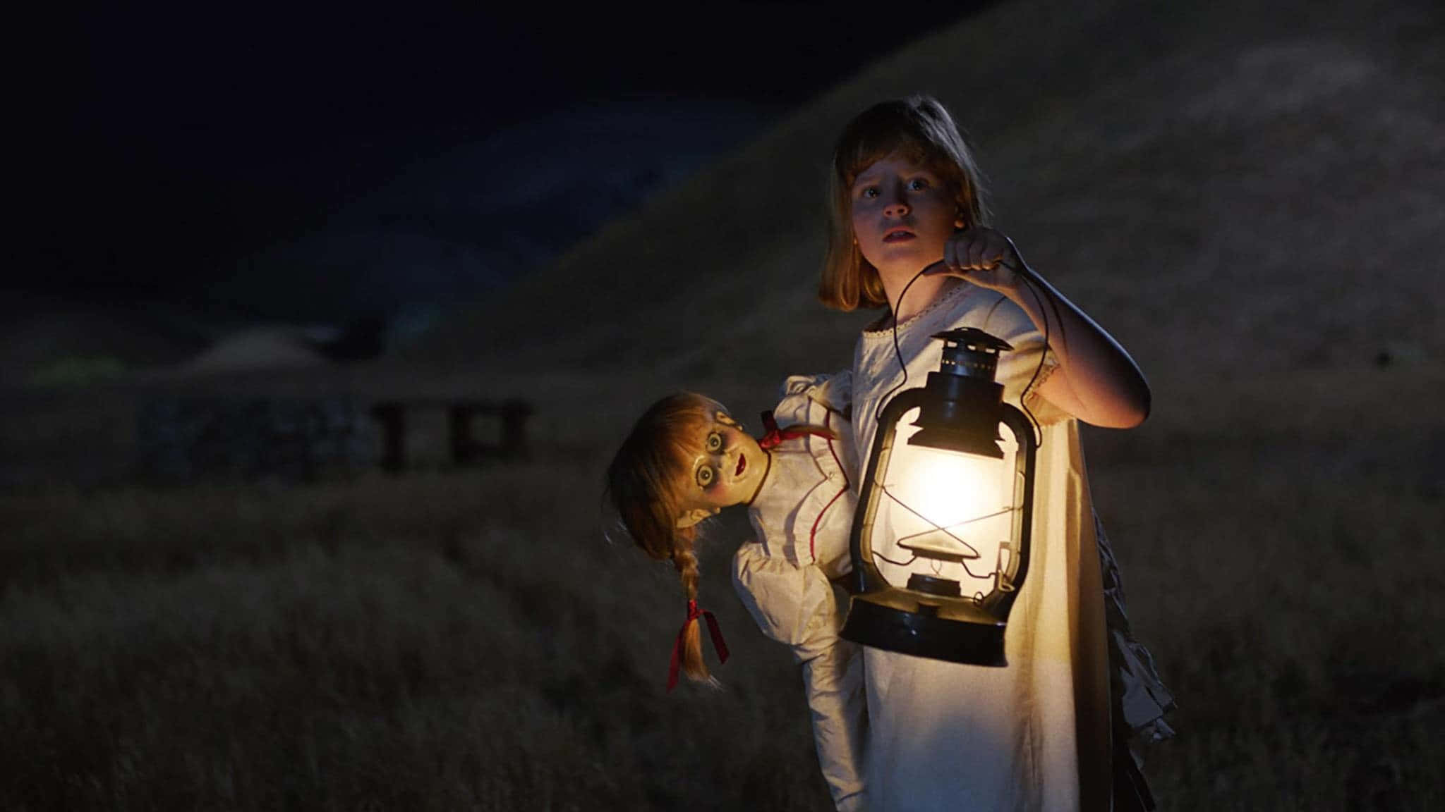 Annabelle 桌布 壁紙 — 一個穿著白色連衣裙的小女孩在夜晚的黑暗草地上拿著發光的燈籠和一個令人毛骨悚然的娃娃。
