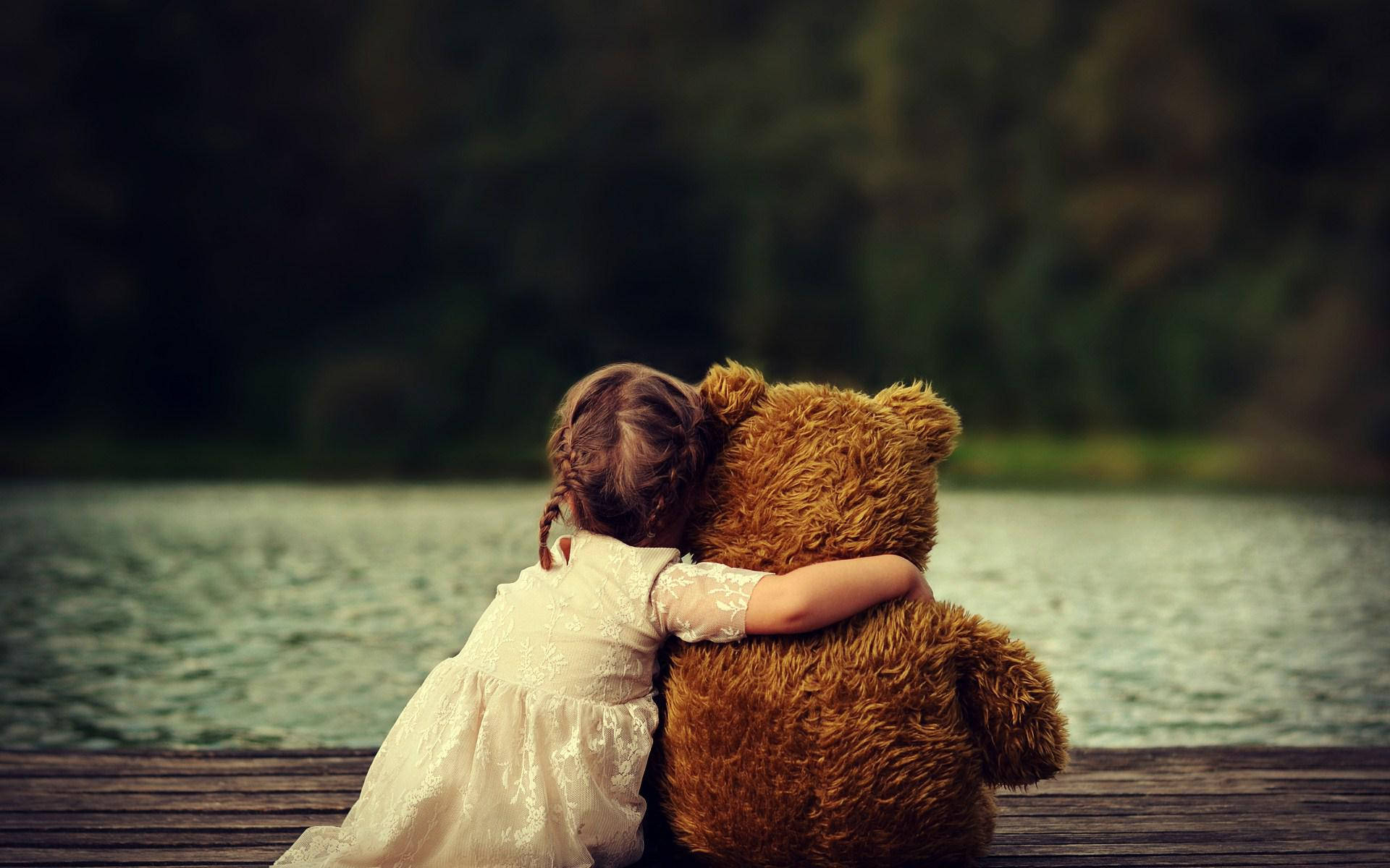 Cute Bear 桌布 壁紙 — 一個穿著白色連衣裙的小女孩坐在一個木製碼頭上，俯瞰著平靜的湖泊，擁抱一隻大的棕色泰迪熊。