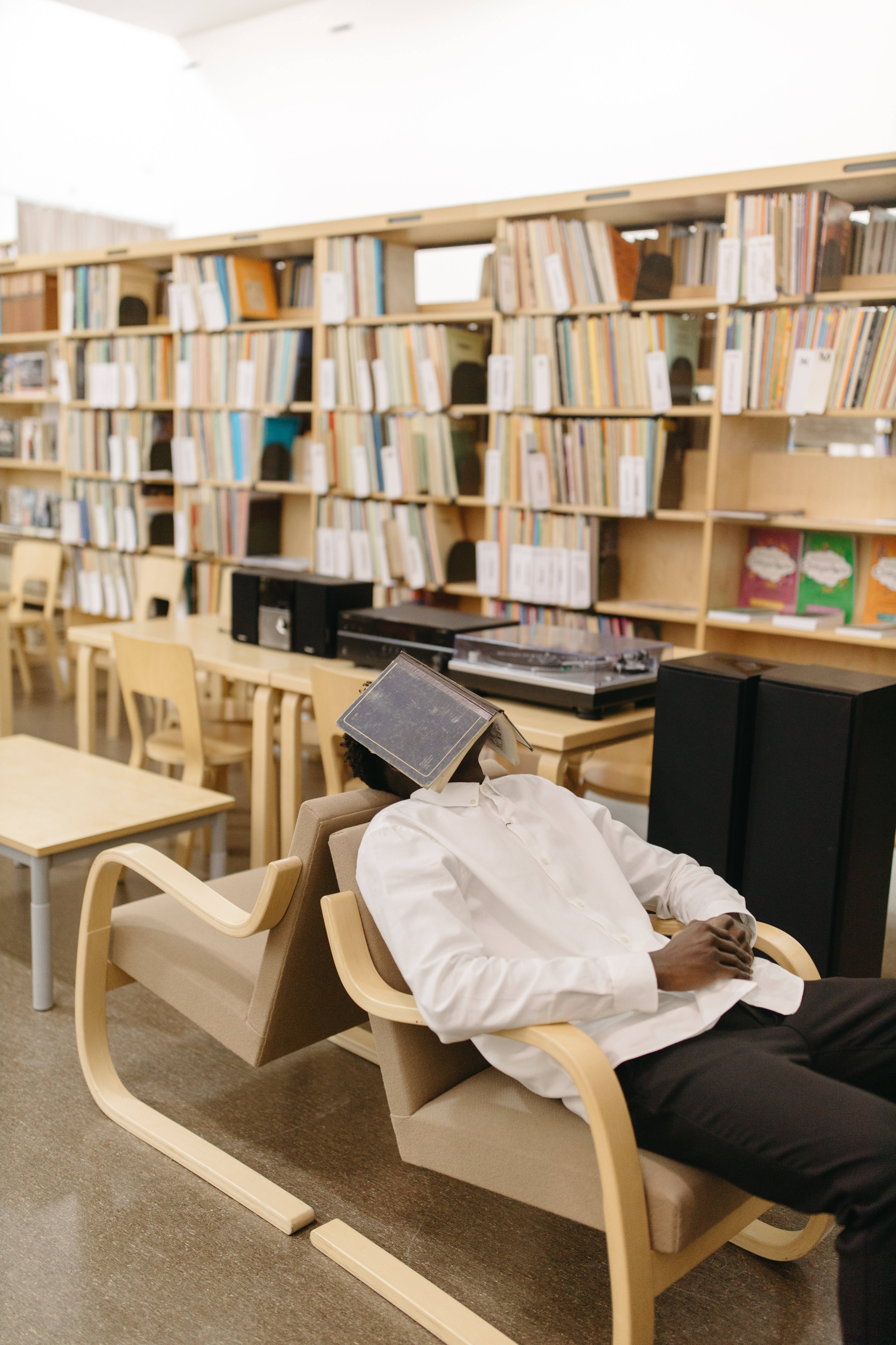 Study 桌布 壁紙 — 一個穿著白襯衫的人，在明亮的圖書館裡，坐在一張現代椅子上睡覺，頭上放著一個復古唱盤。