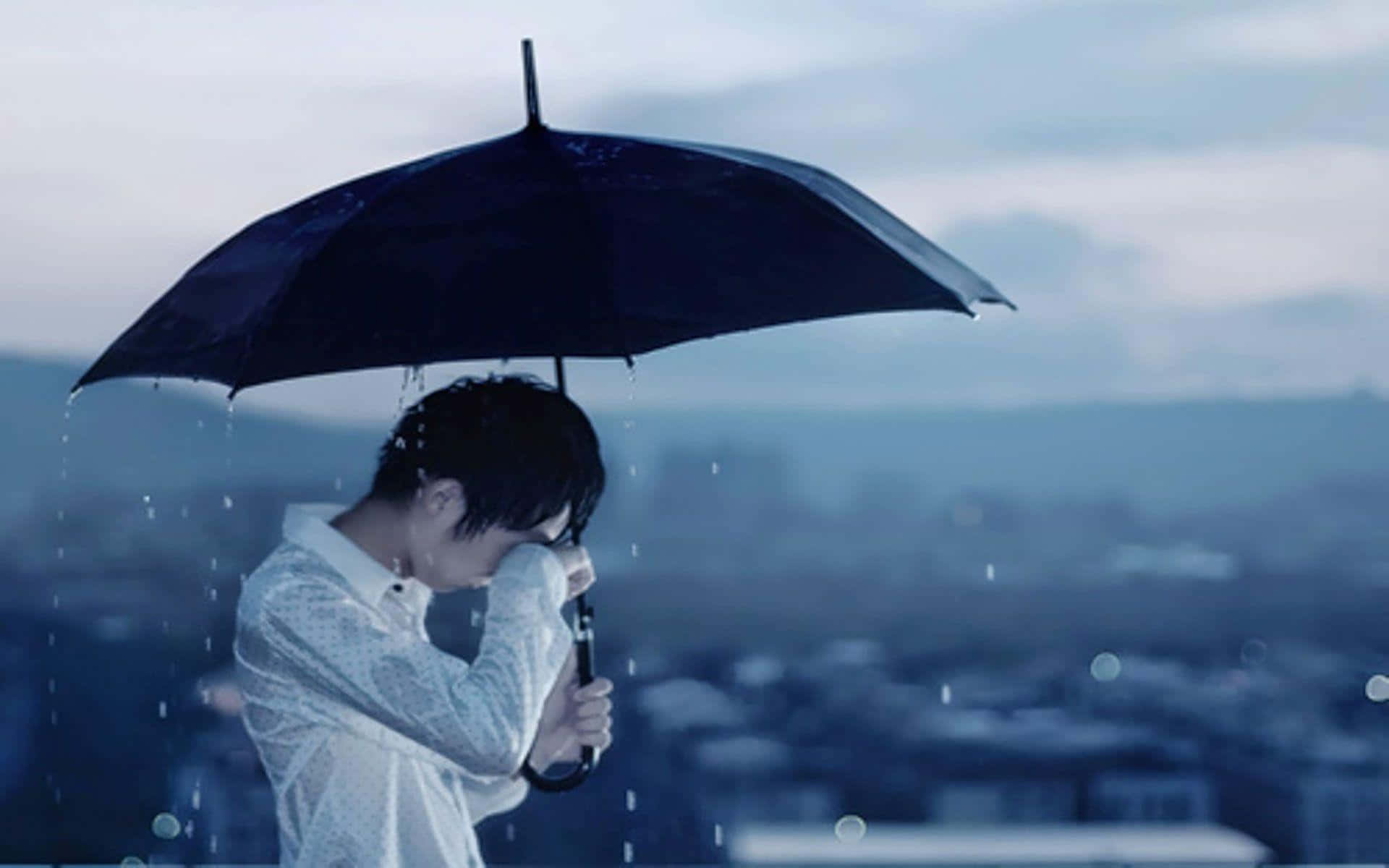 傷心 桌布 壁紙 — 一個穿著白襯衫的人拿著一把黑色雨傘，在模糊的城市天際線背景下遮擋落雨，隱藏自己的臉。