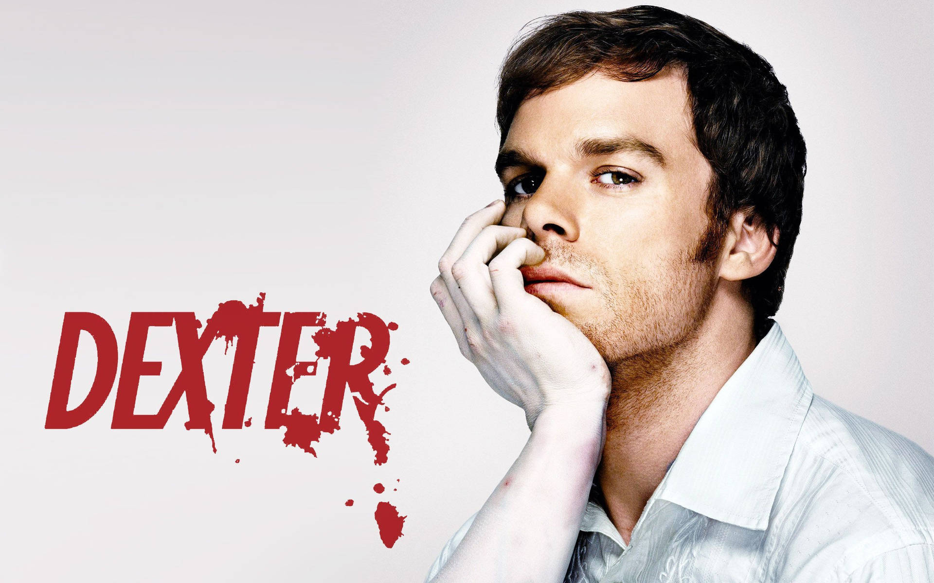 穿著白襯衫的男人，在有紅色濺墨的「Dexter」文字旁邊，表情嚴肅。 — 神秘 壁紙