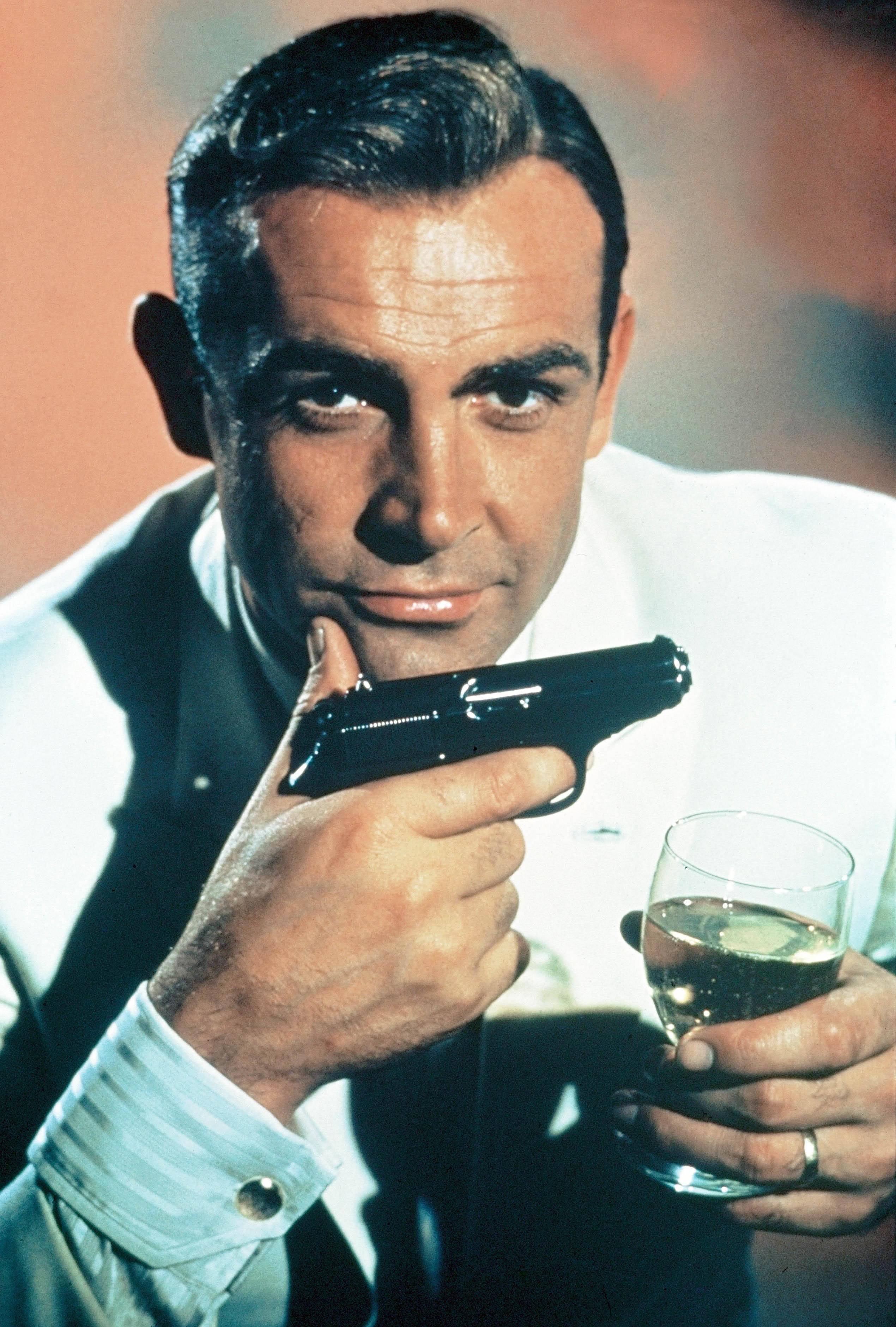 Sean Connery 桌布 壁紙 — 一個穿著白襯衫的男人，自信地拿著一把槍和一杯香檳。