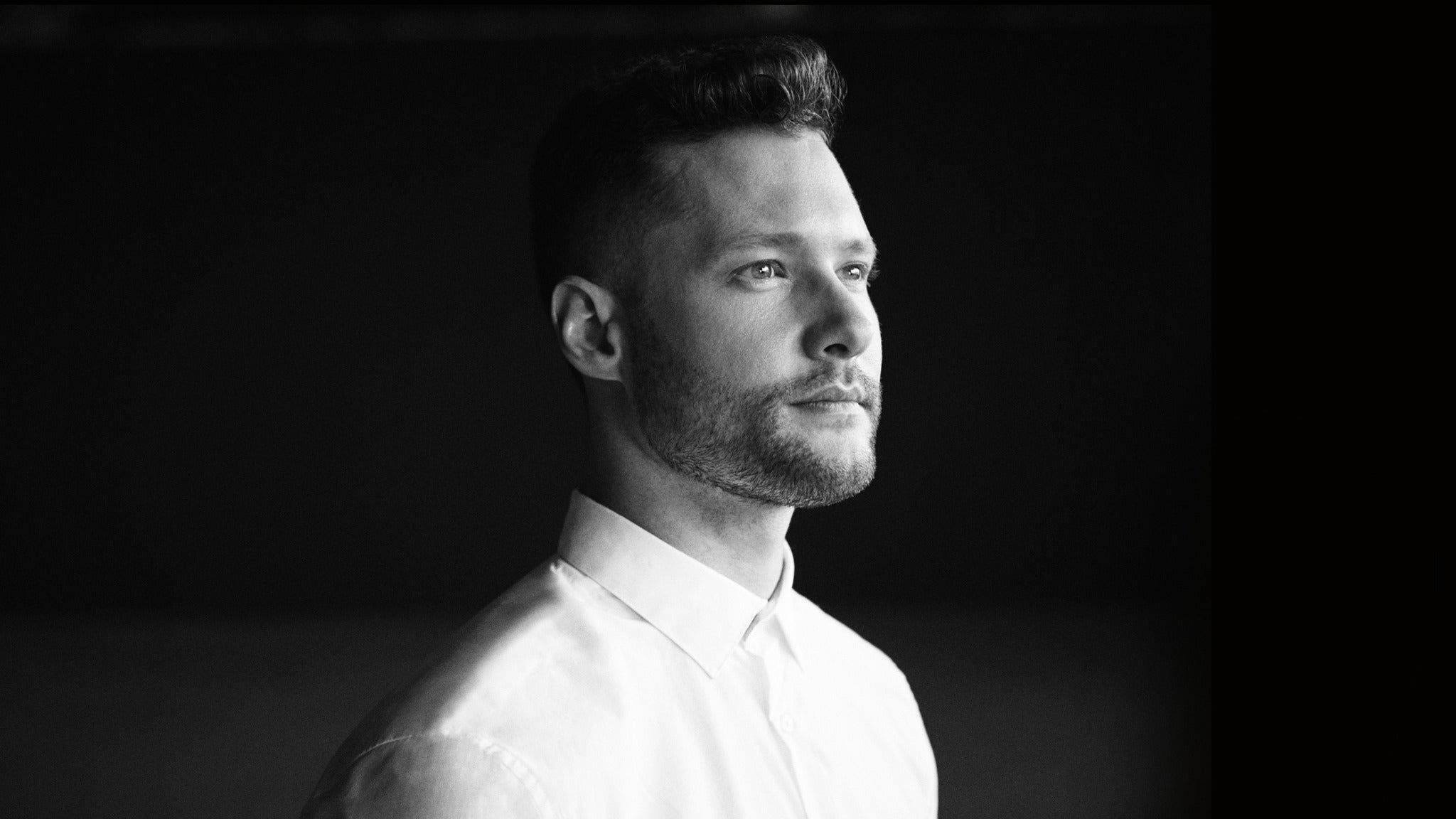 Calum Scott 桌布 壁紙 — 一個穿著白襯衫的男人在深色背景下沉思凝視的黑白肖像。