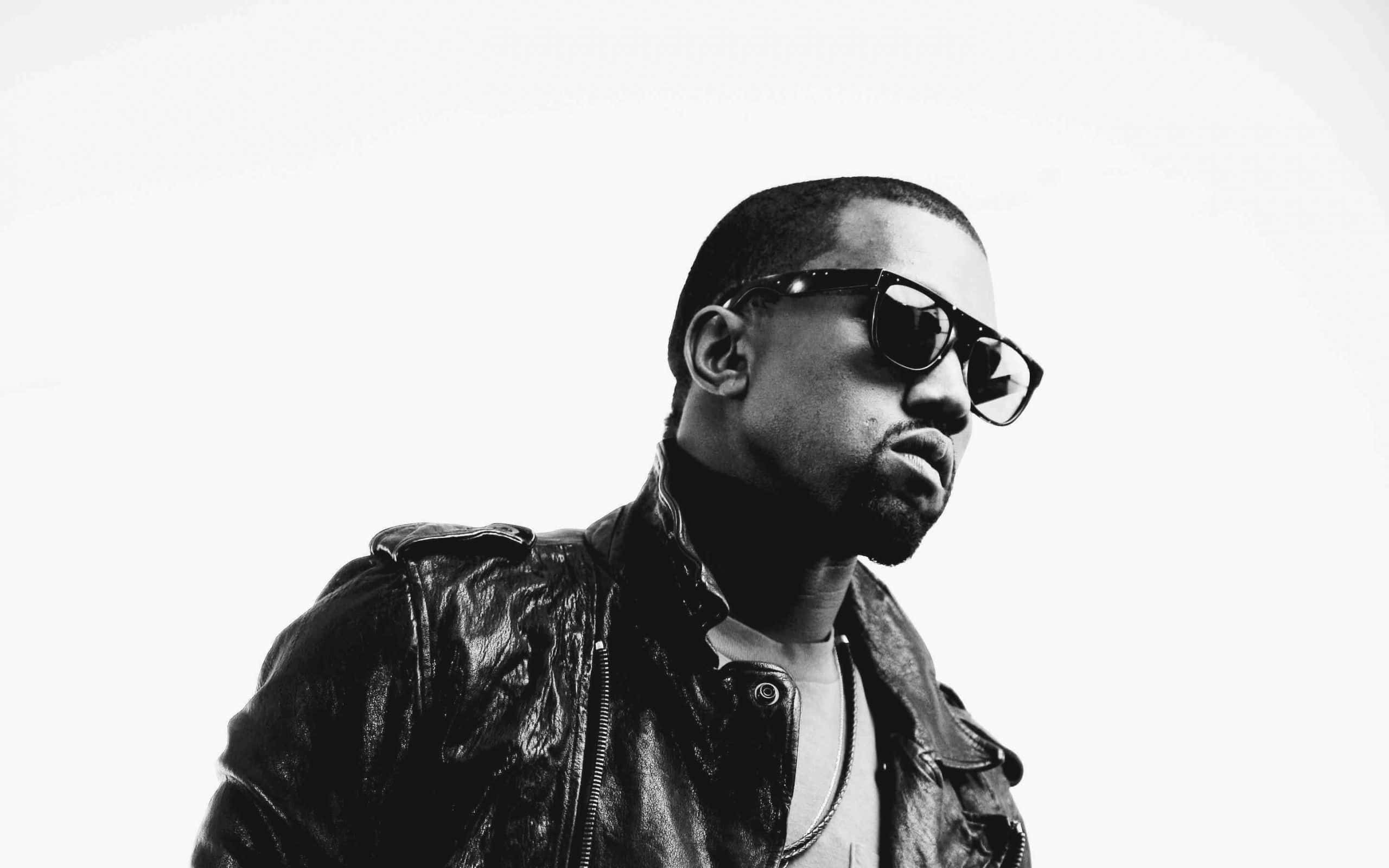 Kanye 桌布 壁紙 — 一個穿著皮夾克和太陽眼鏡的男人，在純白背景前以高對比黑白風格凝視。