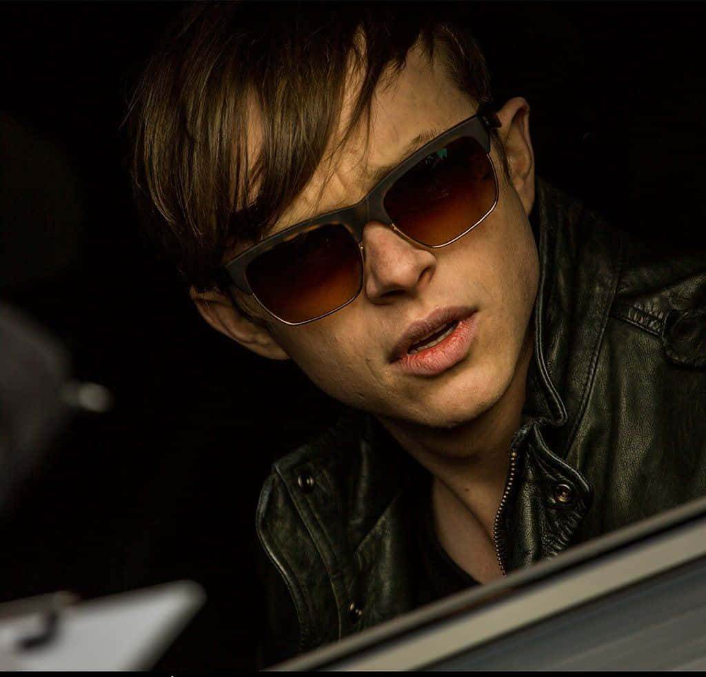 Harry Osborn 桌布 壁紙 — 一個穿著皮夾克和深色太陽眼鏡的年輕男子，在昏暗的車內向前傾，表情嚴肅。