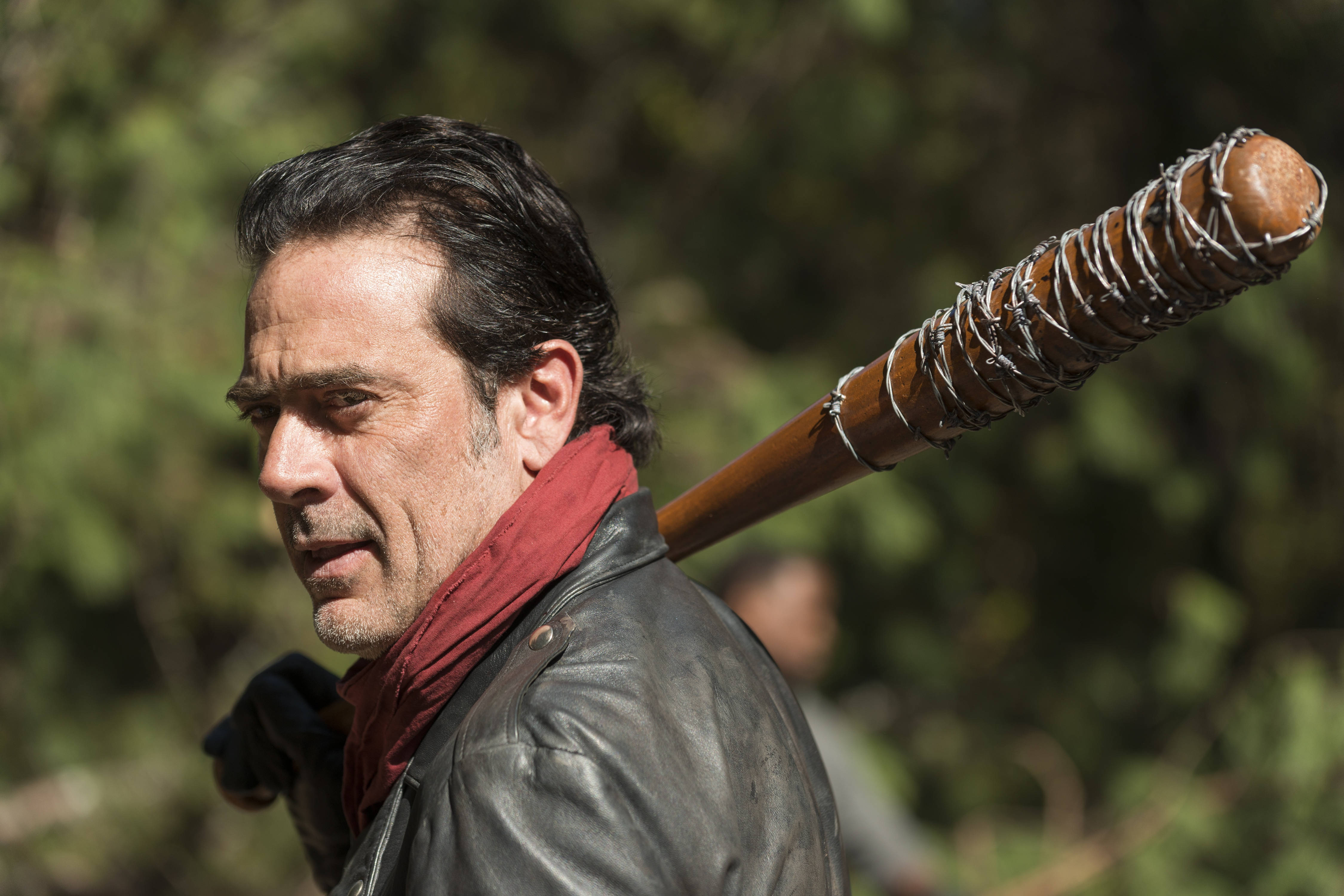 Negan 桌布 壁紙 — 一個穿著皮夾克的男人，肩上扛著一支帶有鐵絲網的棒球棍，穿過陽光明媚的森林。