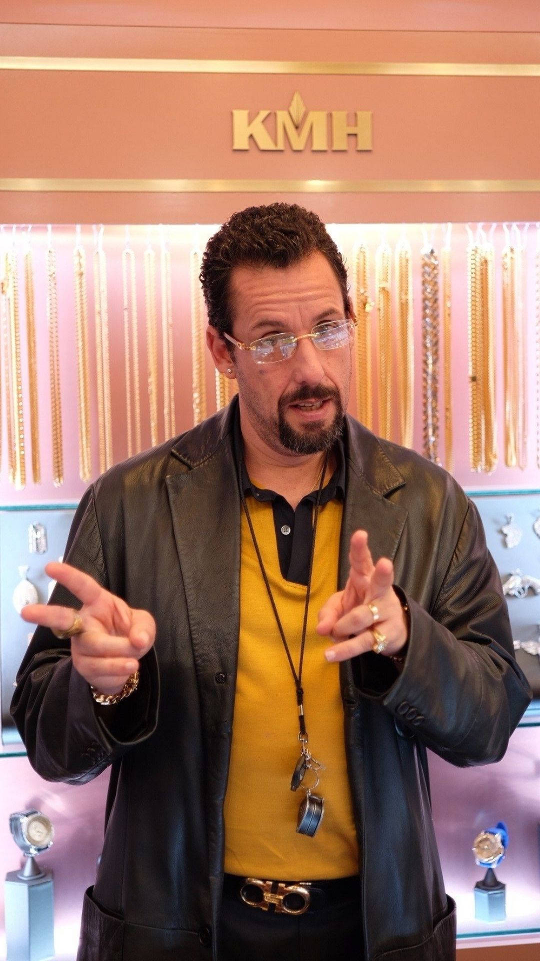 Adam Sandler 桌布 壁紙 — 一個穿著皮夾克的男人在一間珠寶店內生動地做手勢，他後面展示著金鍊。