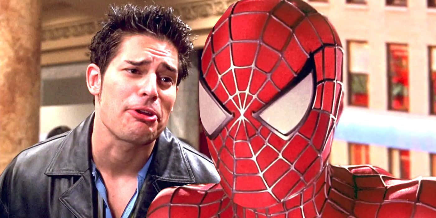Flash Thompson 桌布 壁紙 — 一個穿著皮夾克的男人站在城市環境中，旁邊是一件紅藍色的蜘蛛人戰衣。